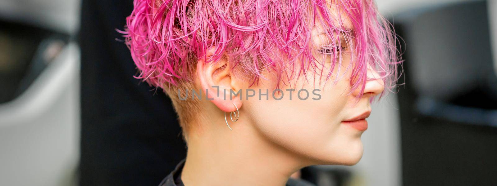 Beautiful young caucasian woman receiving new short pink hairstyle in hairdresser salon