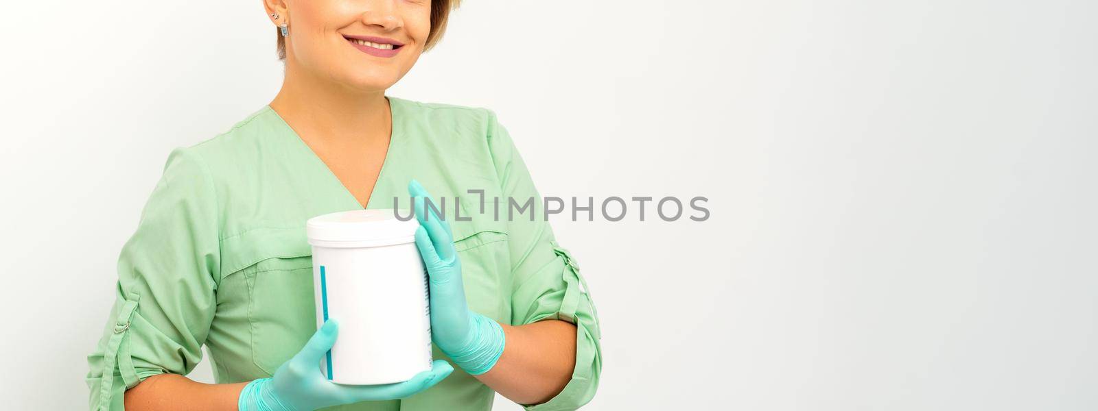 Cosmetics creams and skin care products in the hands of the female beautician smiling and standing over the white wall background