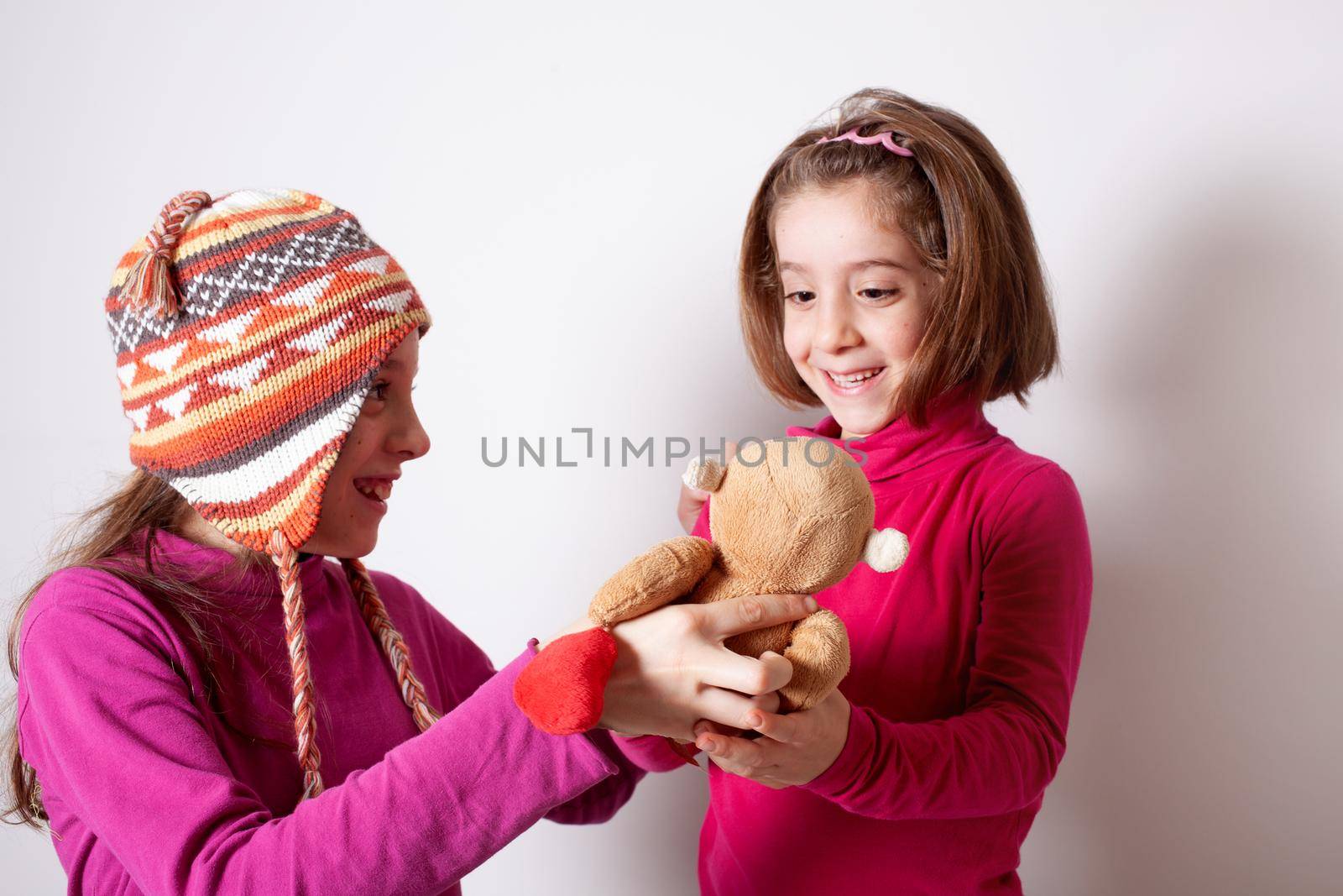 Little girl giving her teddy bear toy to younger sister. Cute child girl giving a gift to her sister. by bepsimage