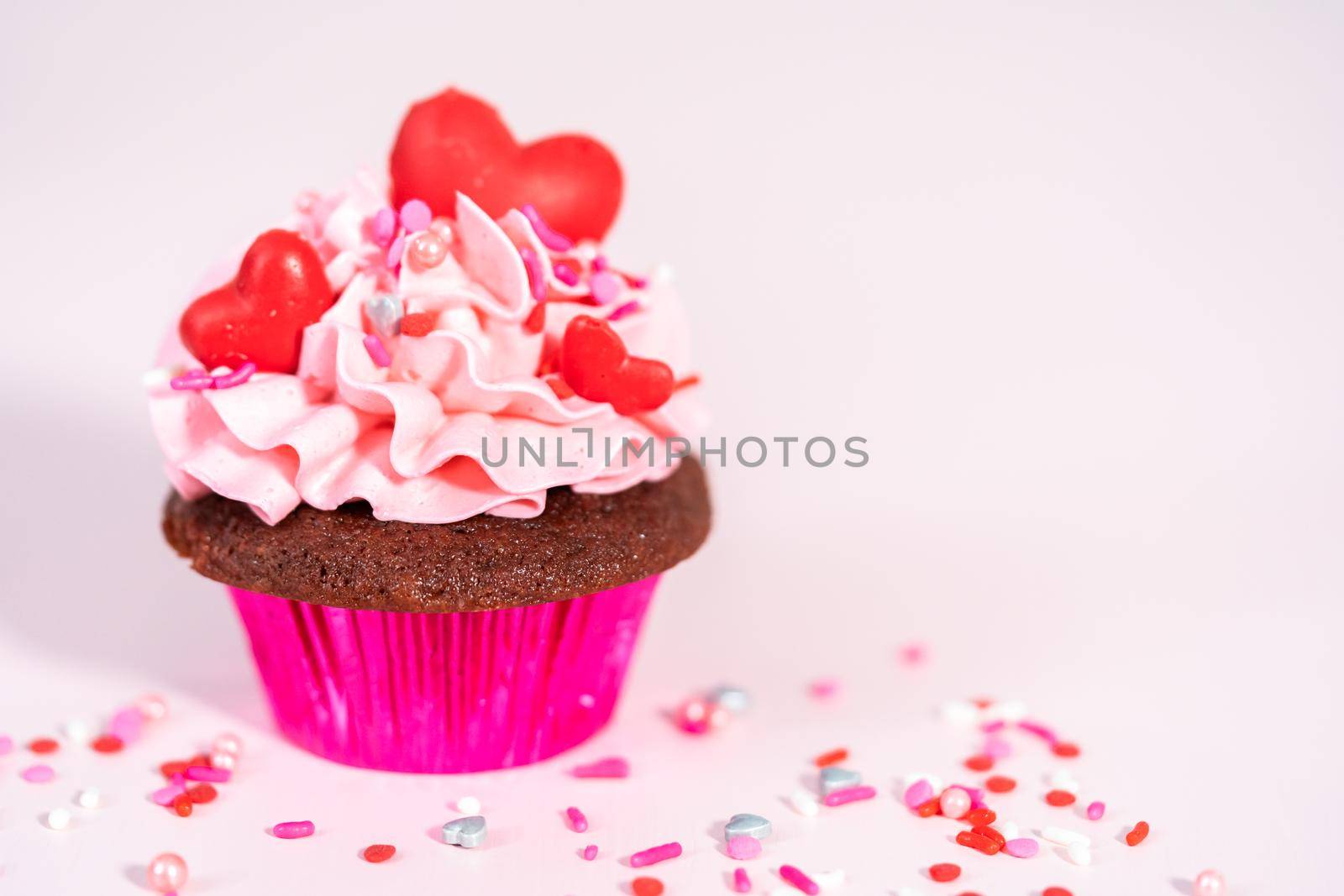 Red velvet cupcakes with pink Italian buttercream frosting and decorates with heart and kiss shaped red chocolates.
