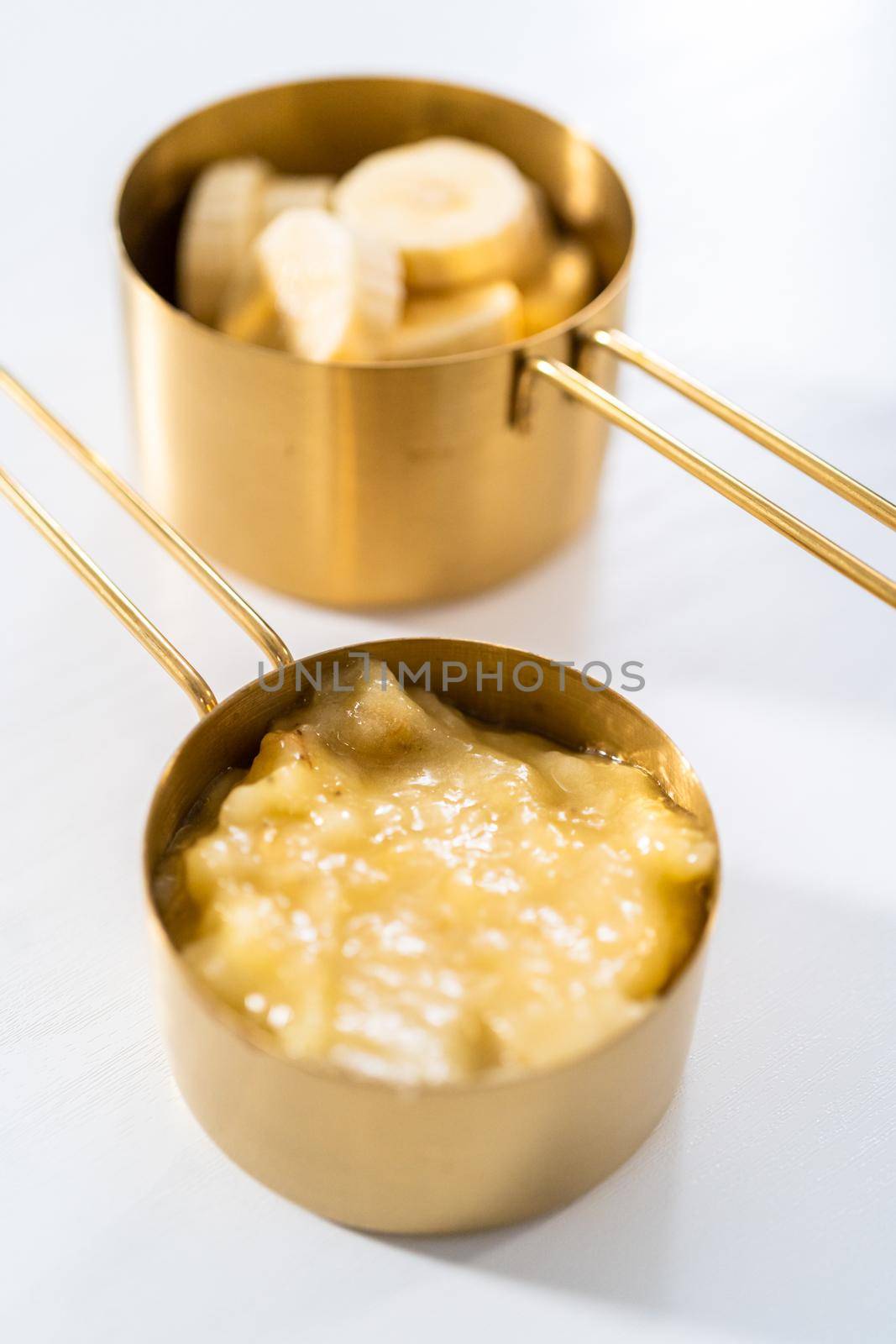 Mashed overripe bananas and sliced riped bananas in metal measuring cups.