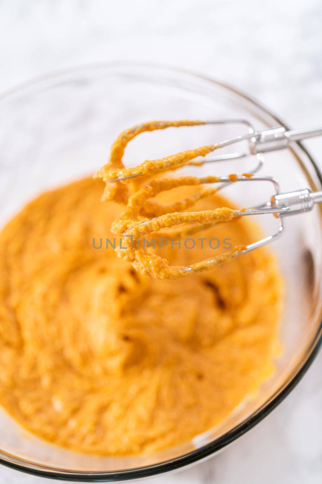 Mixing ingredients in a large glass mixing bowl to bake pumpkin bunt cake.