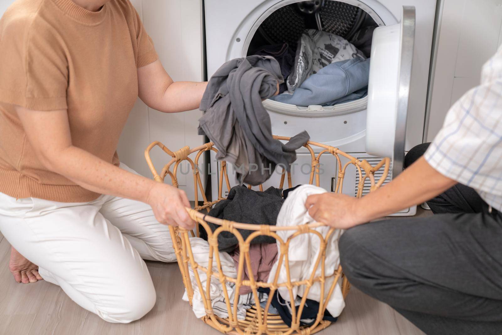 Senior couple working together to complete their household chores at the washing machine in a happy and contented manner. Husband and wife doing the usual tasks in the house.