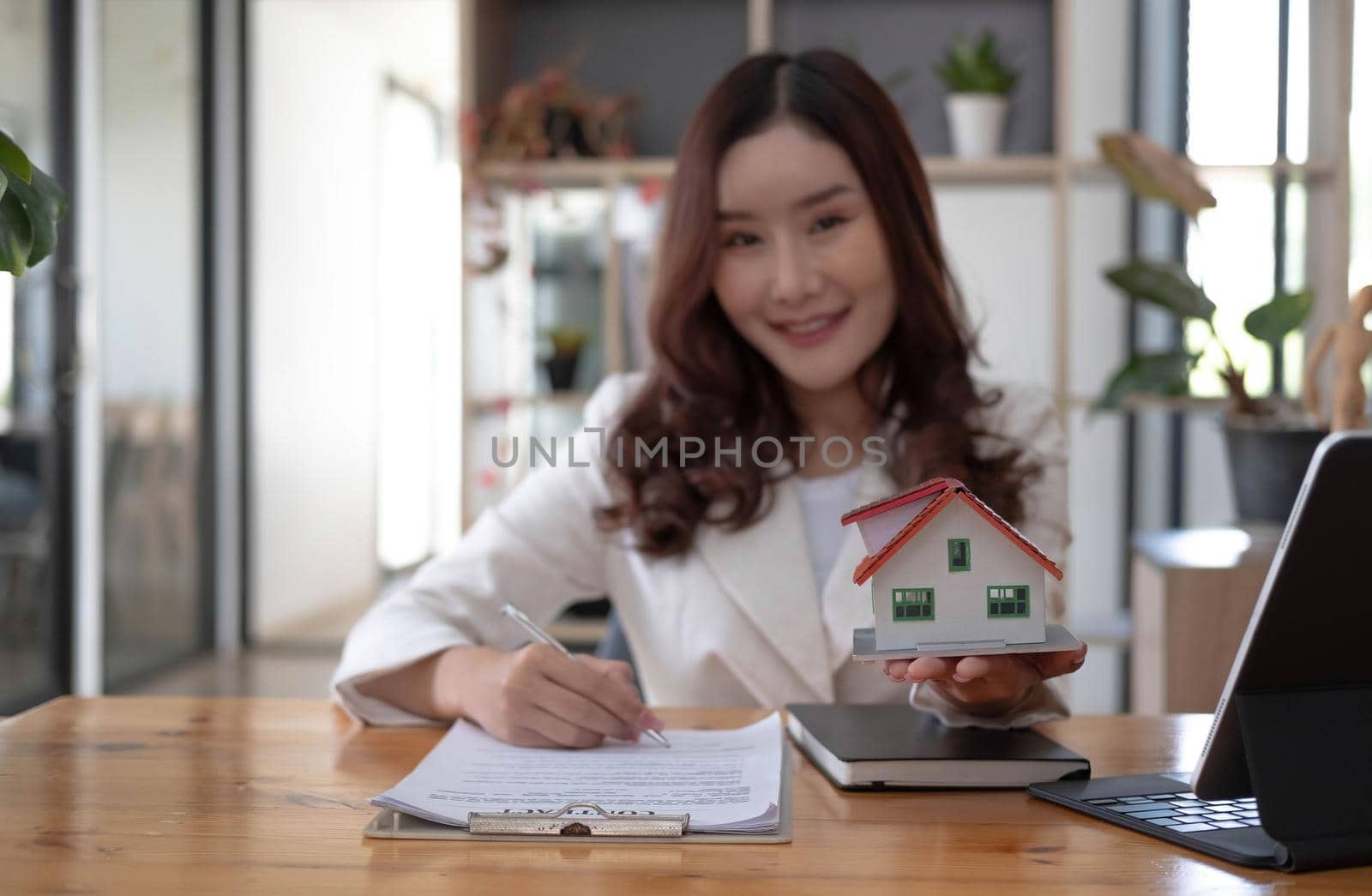 Miniature house in the hands of an Asian woman real estate agent home loan working at the office. Looking at the camera..