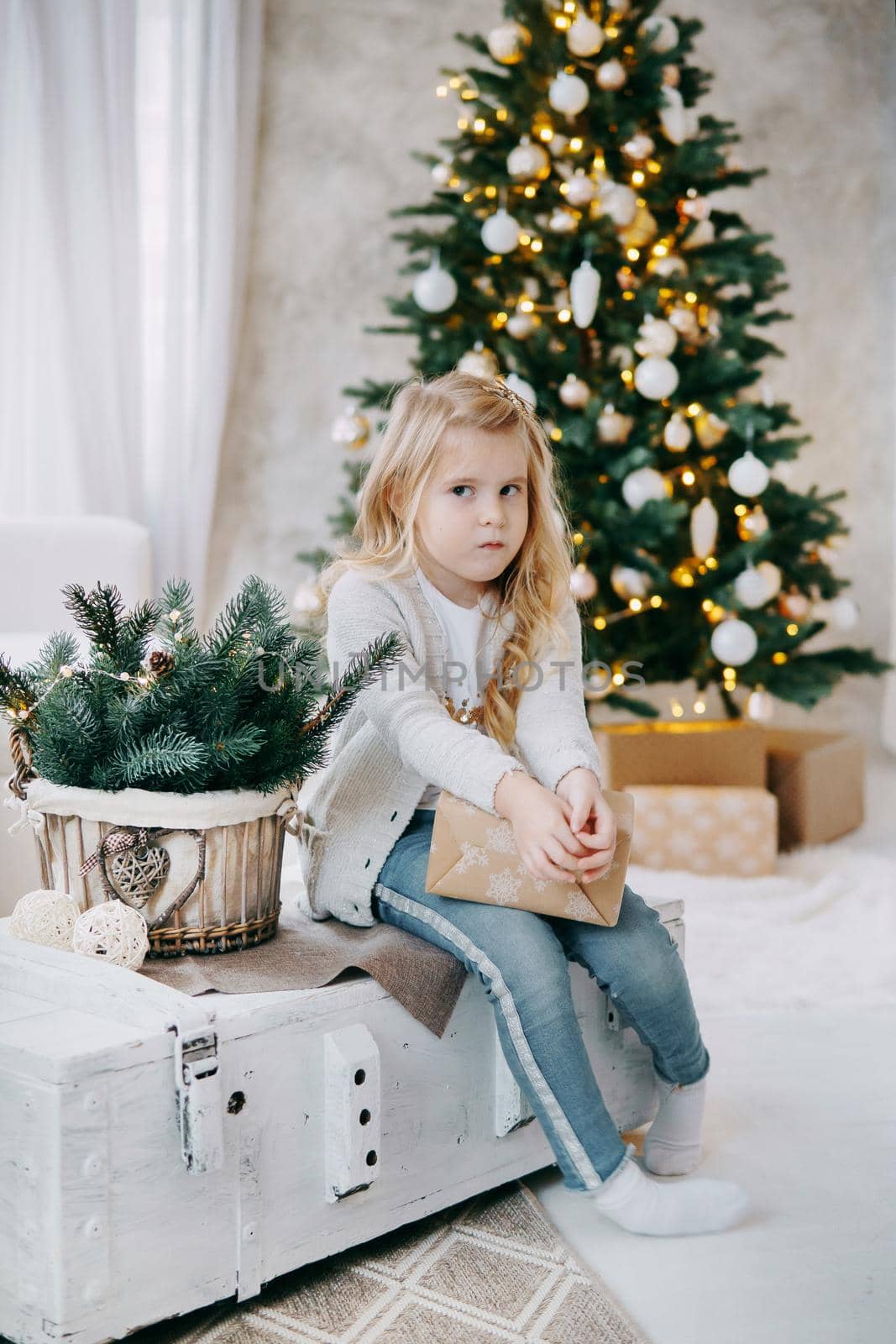 A blonde girl with a Christmas gift in her hands, on the background of a Christmas tree.The concept of New Year's decor and New Year's holidays.