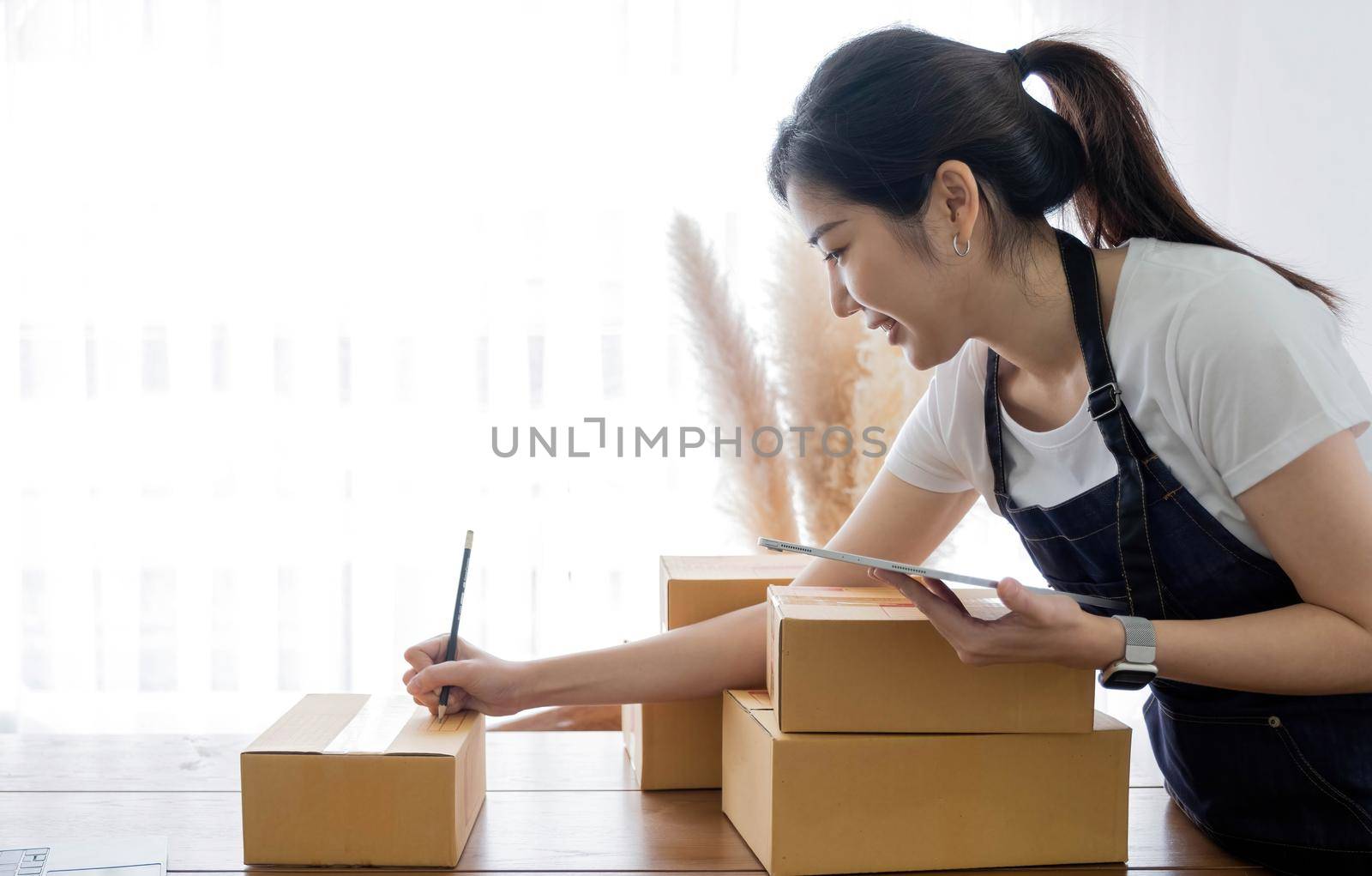 Portrait of Asian young woman SME working with a box at home the workplace.start-up small business owner, small business entrepreneur SME or freelance business online and delivery concept. by wichayada