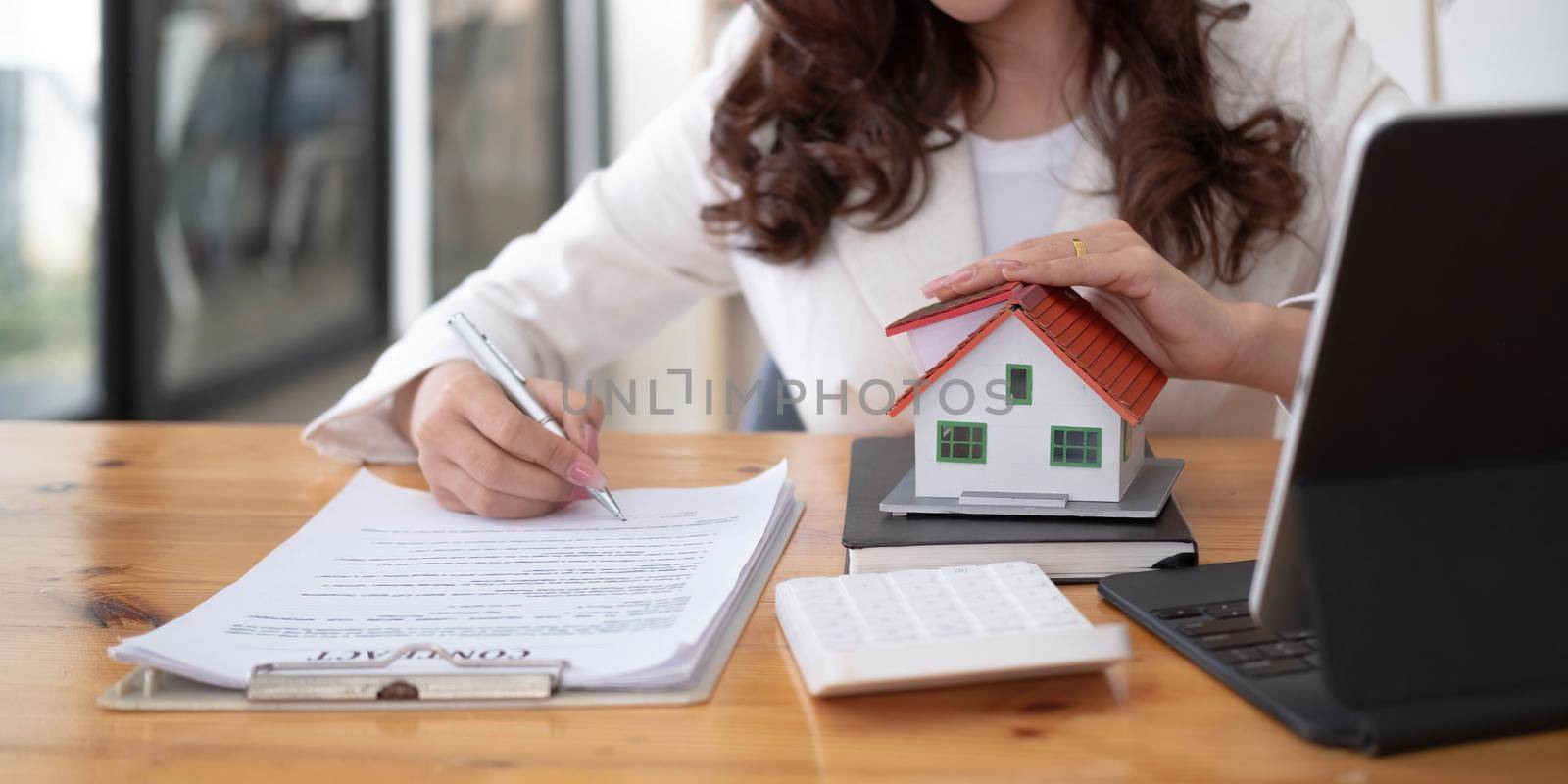 Close up of woman hands holding home model, Real estate brokerage contracts for sale and rent with insurance loan mortgage concepts..