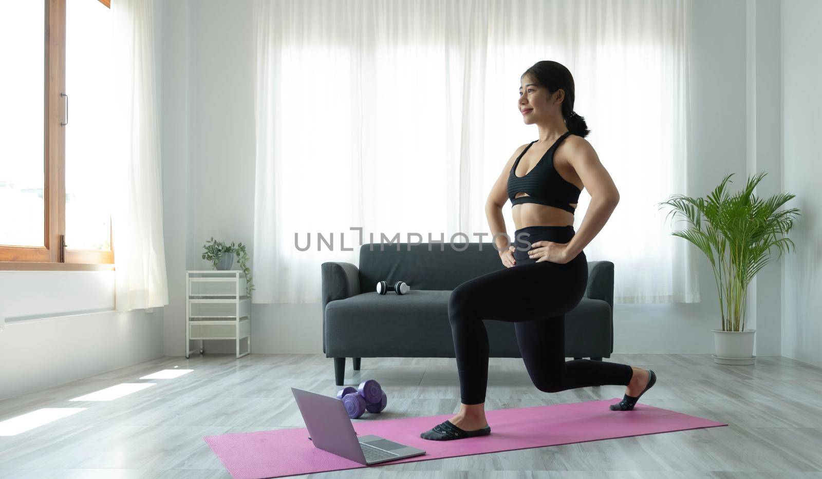 Smiling Asian woman doing yoga shoulder stretching online class from laptop at home in living room. Self isolation and workout at home..