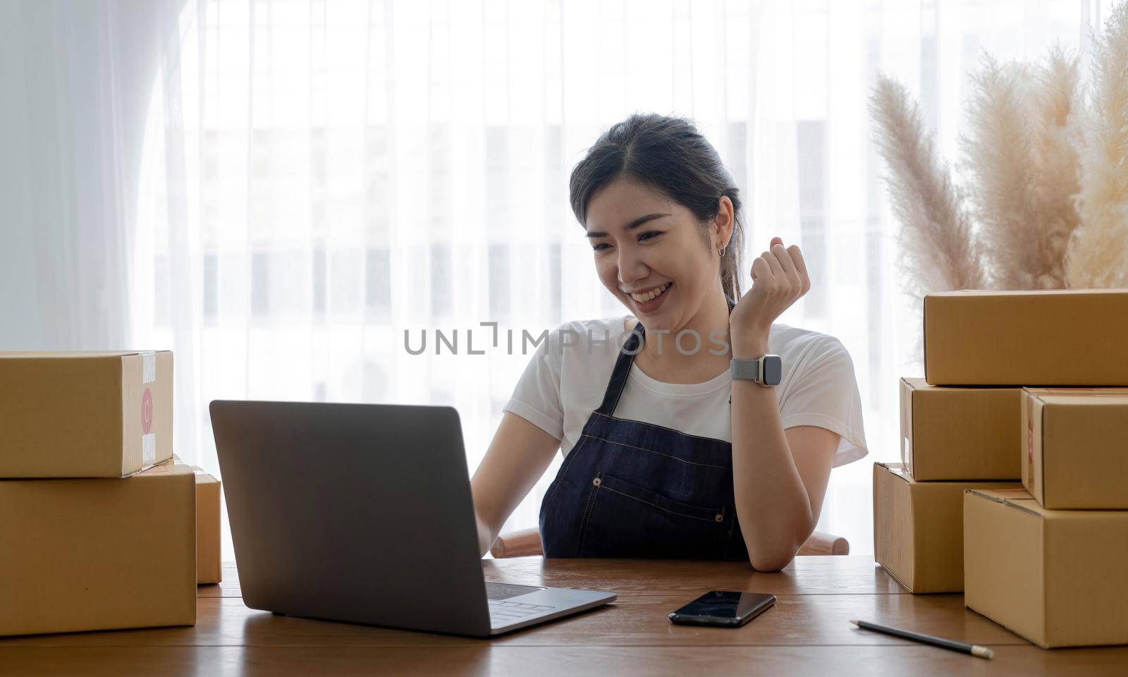 Startup SME small business entrepreneur of freelance Asian woman using a laptop with box Cheerful success Asian woman her hand lifts up online marketing packaging box and delivery SME idea concept.