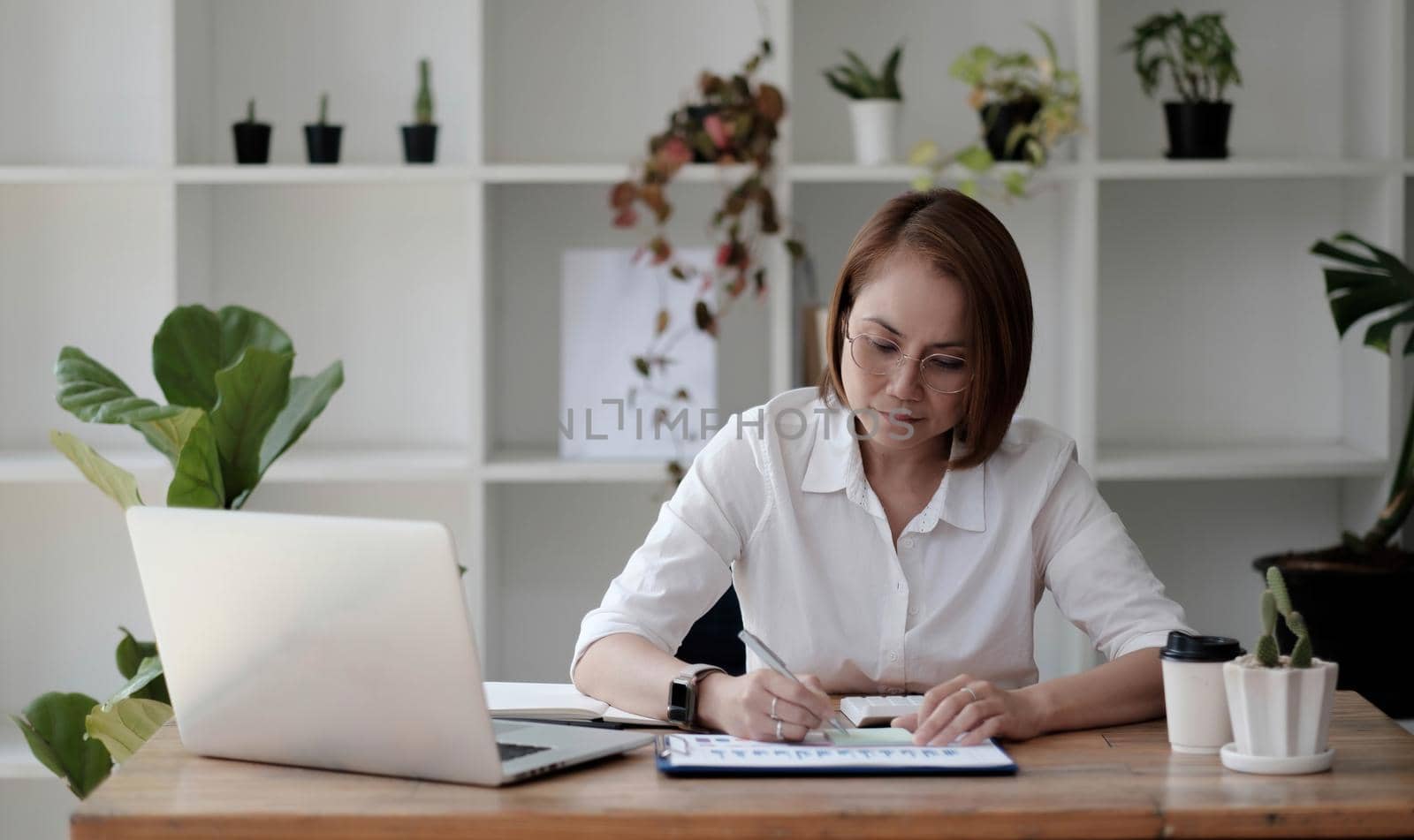 Serious focused Asian older 40s businesswoman executive manager sitting at desk working typing on pc laptop computer in contemporary office. Business online technology concept..