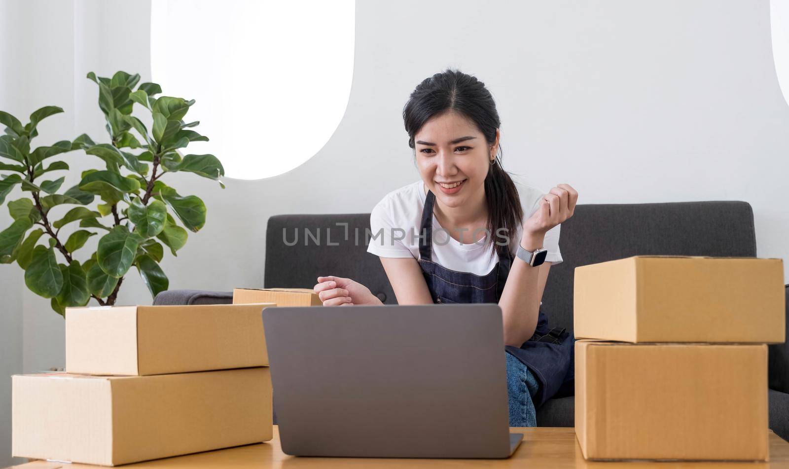 Startup SME small business entrepreneur of freelance Asian woman using a laptop with box Cheerful success Asian woman her hand lifts up online marketing packaging box and delivery SME idea concept.