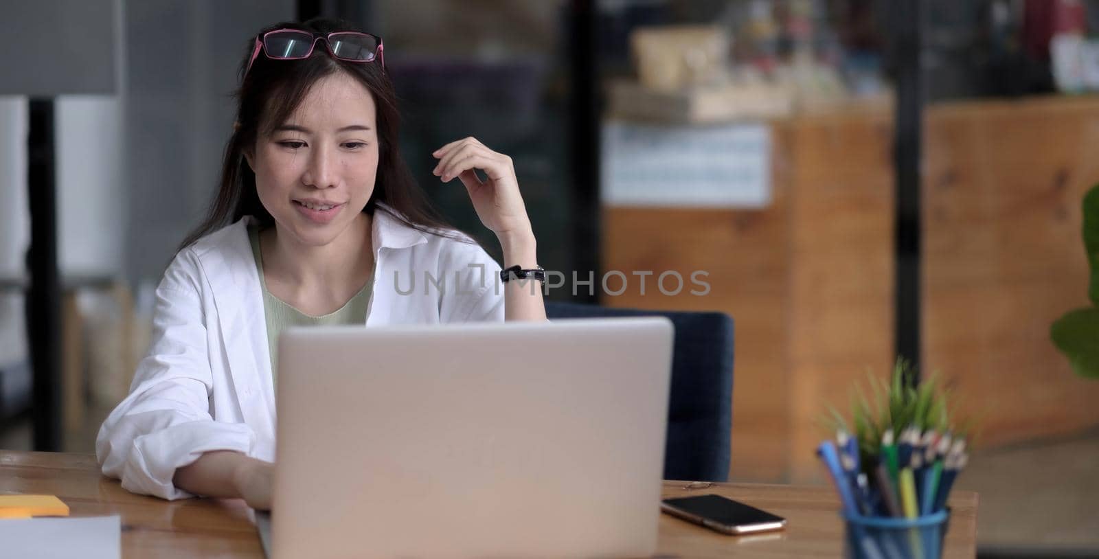 Charming asian businesswoman sitting working on laptop in office. by wichayada