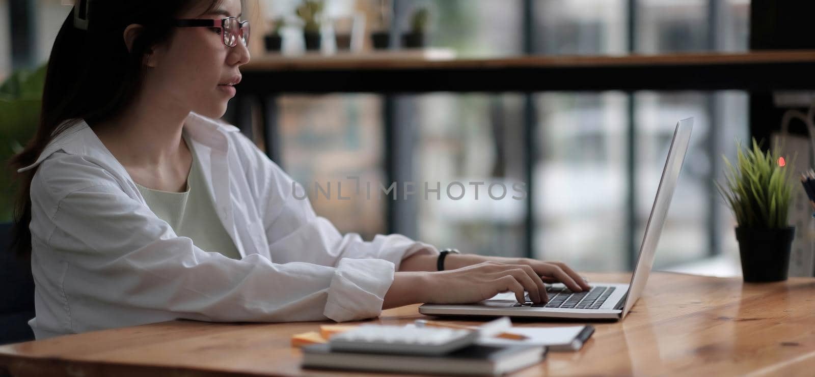 Beautiful young asian woman sitting at coffee shop using laptop. Happy young businesswoman sitting at table in cafe with tab top computer. by wichayada