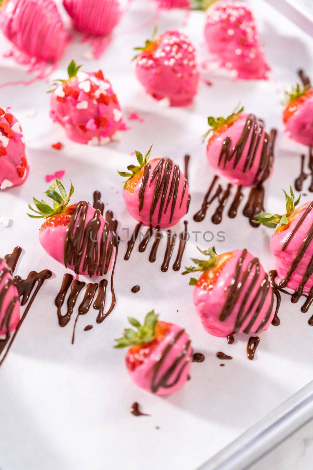 Decorating chocolate-covered strawberries with chocolate drizzles and sprinkles.