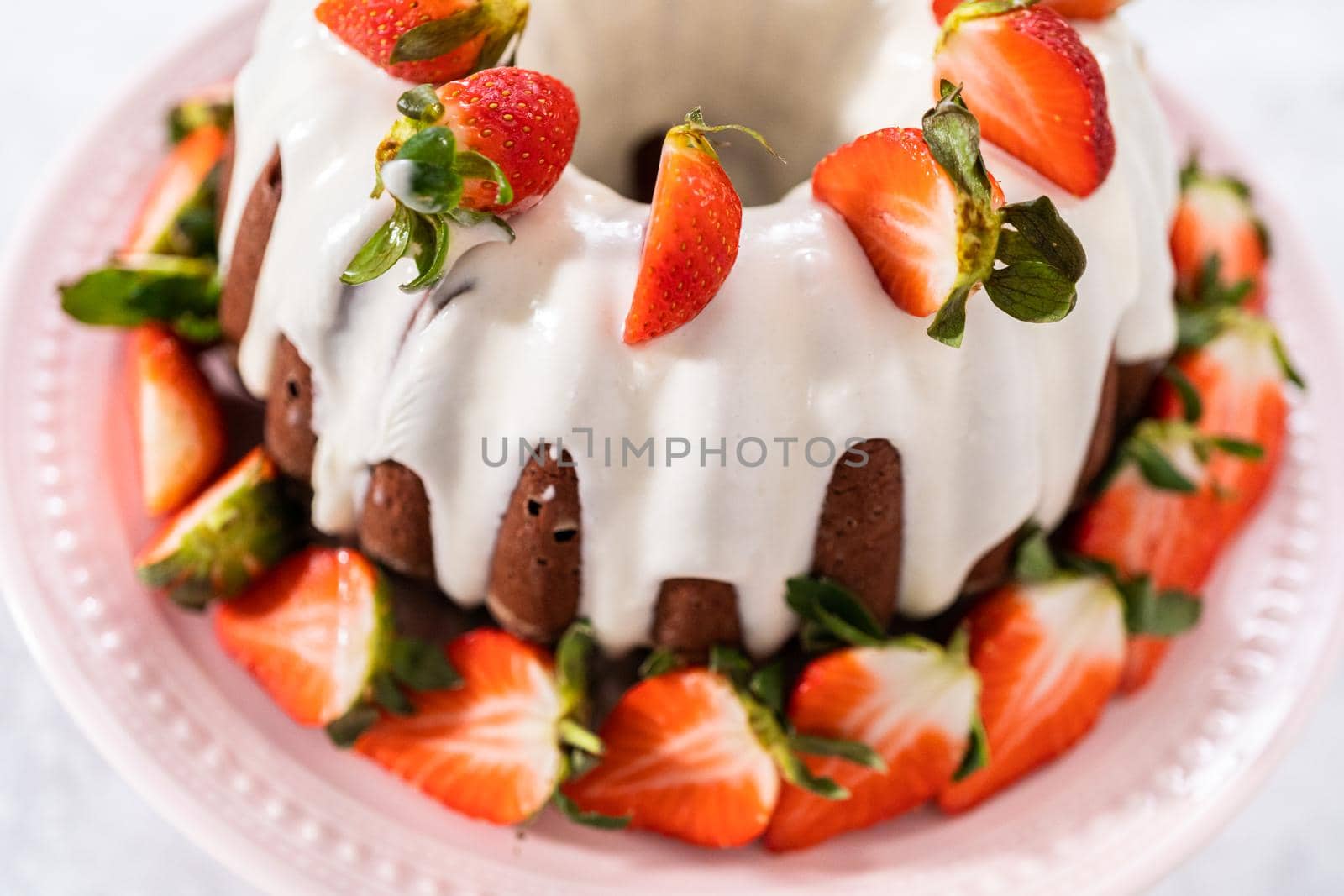 fresh strawberries..Red velvet bundt cake with cream cheese frosting garnished with fresh strawberries on a pink cake stand for Valentines Day.