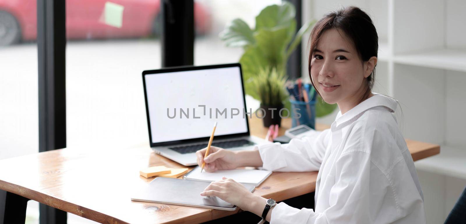 Charming Asian woman working at the office using a laptop Looking at the camera. by wichayada