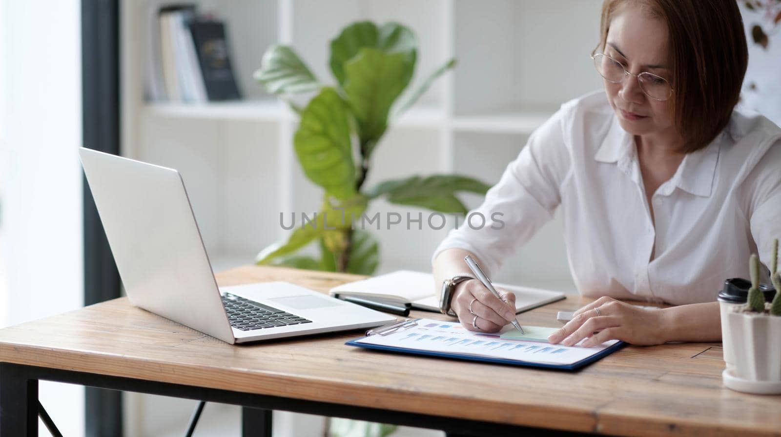 Serious focused Asian older 40s businesswoman executive manager sitting at desk working typing on pc laptop computer in contemporary office. Business online technology concept..