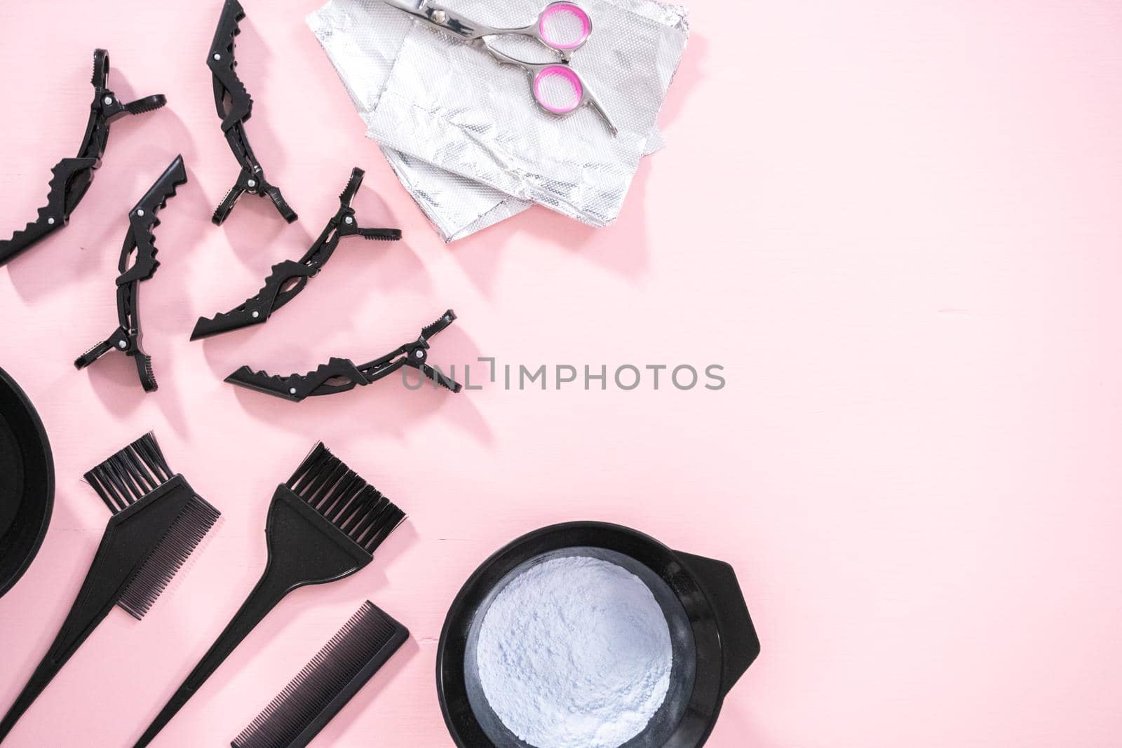 Flat lay. Hair color dye powder in a black plastic mixing bowl on a pink background.