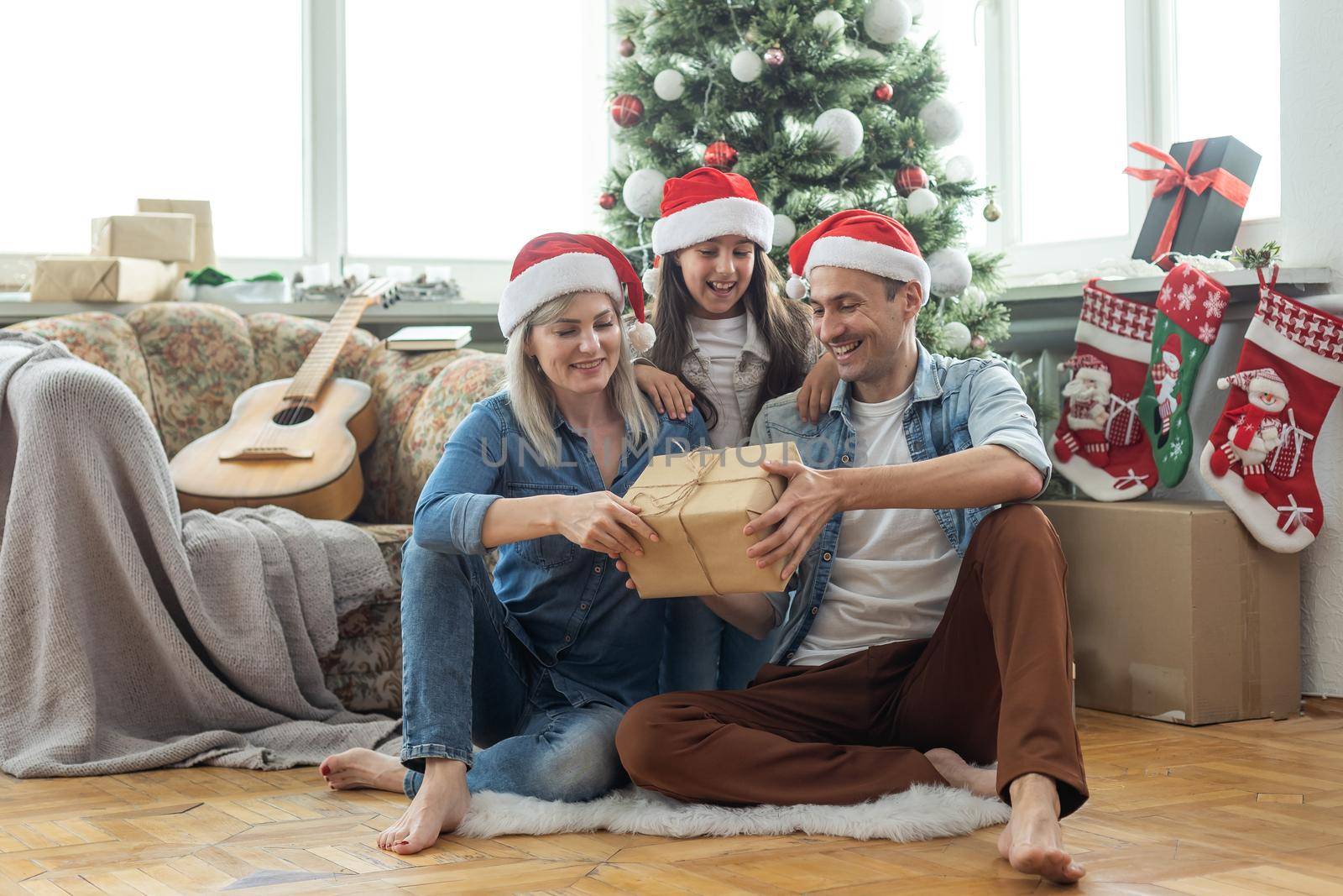 Merry Christmas and Happy New Year. Happy family on the living room floor one after another and laughing near beautiful Christmas tree at home. Happy family and kid by Andelov13