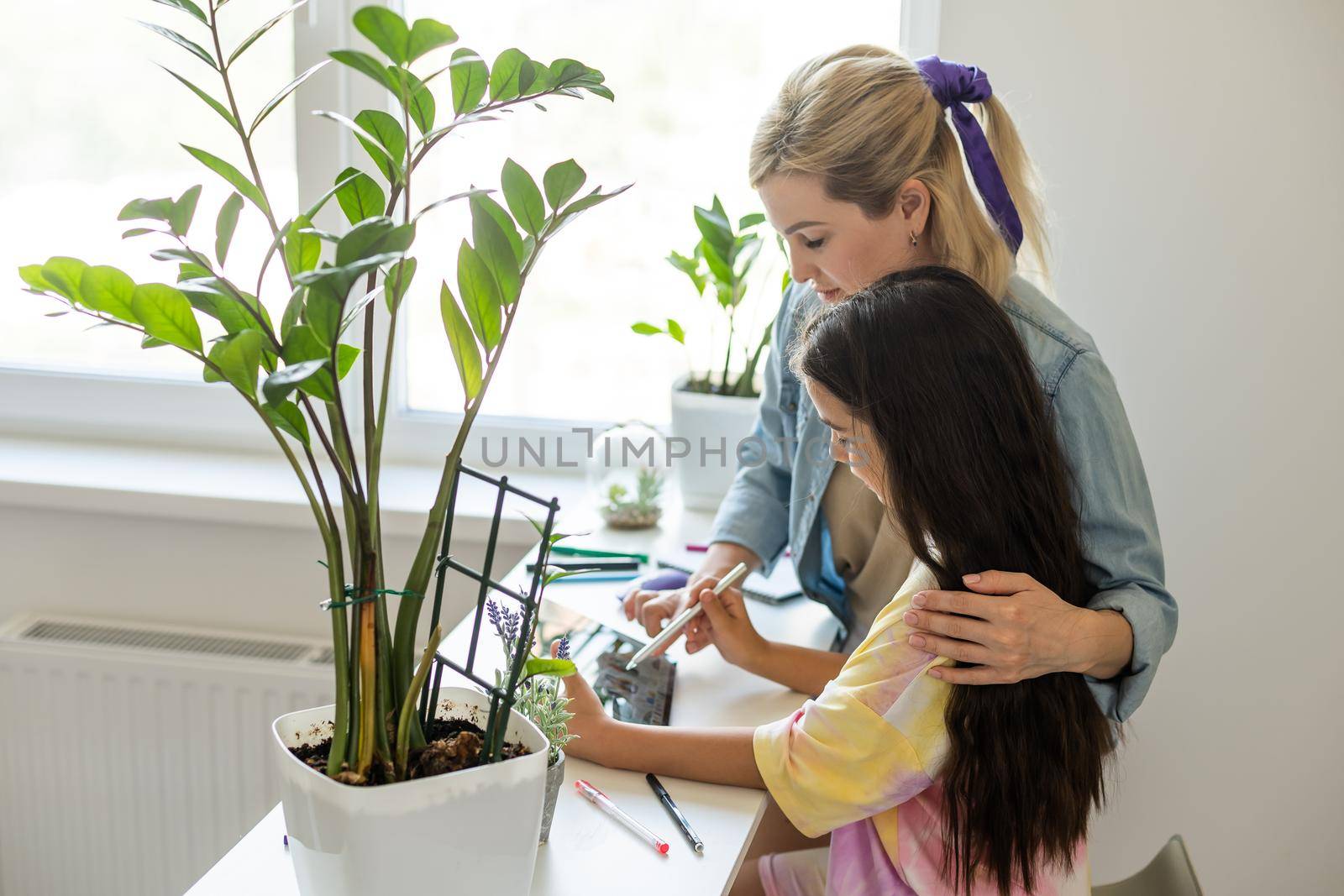 Charming little girl and her beautiful young mom are using a digital tablet and smiling at home by Andelov13