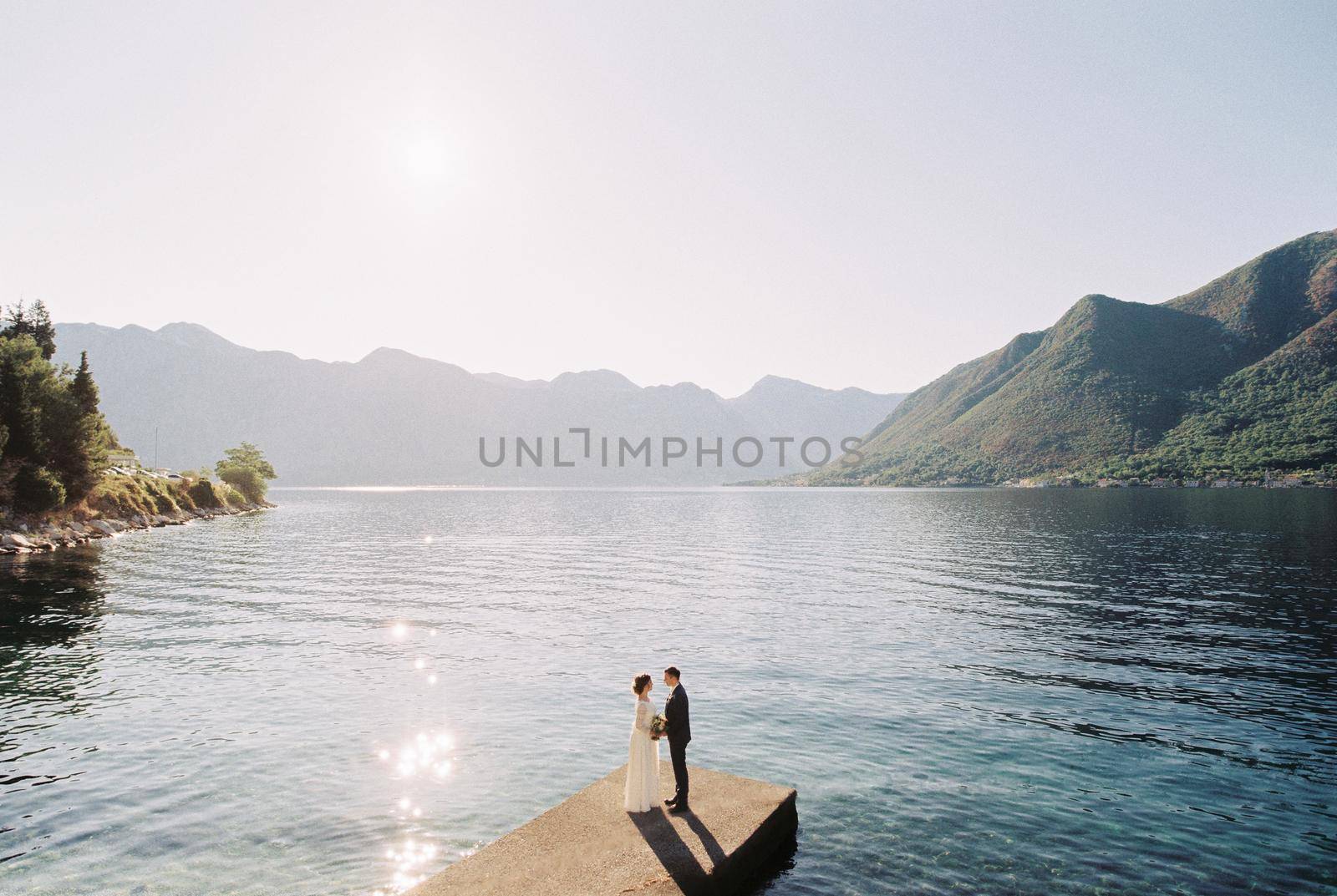 Bride and groom are standing on the pier overlooking the mountain range. High quality photo