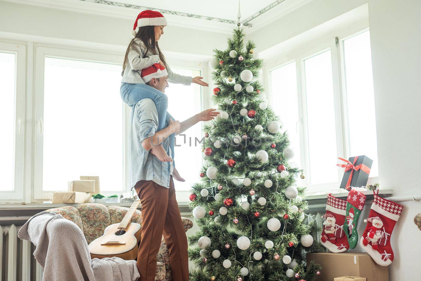 Family decorating a Christmas tree. Young man with his daughter on his shoulders helping her decorate the Christmas tree.