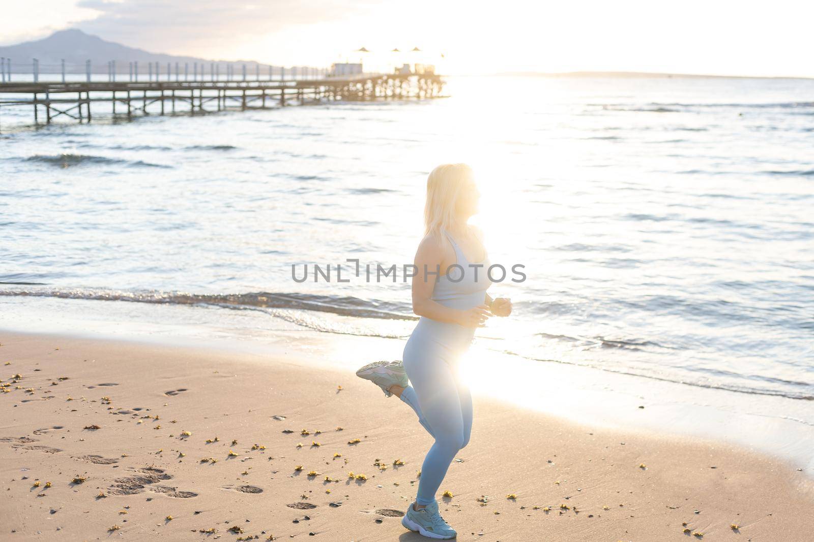 Attractive fit woman practicing side lunges, exercising on the beach on a bright sunny day. Healthy lifestyle, outdoor workout by Andelov13