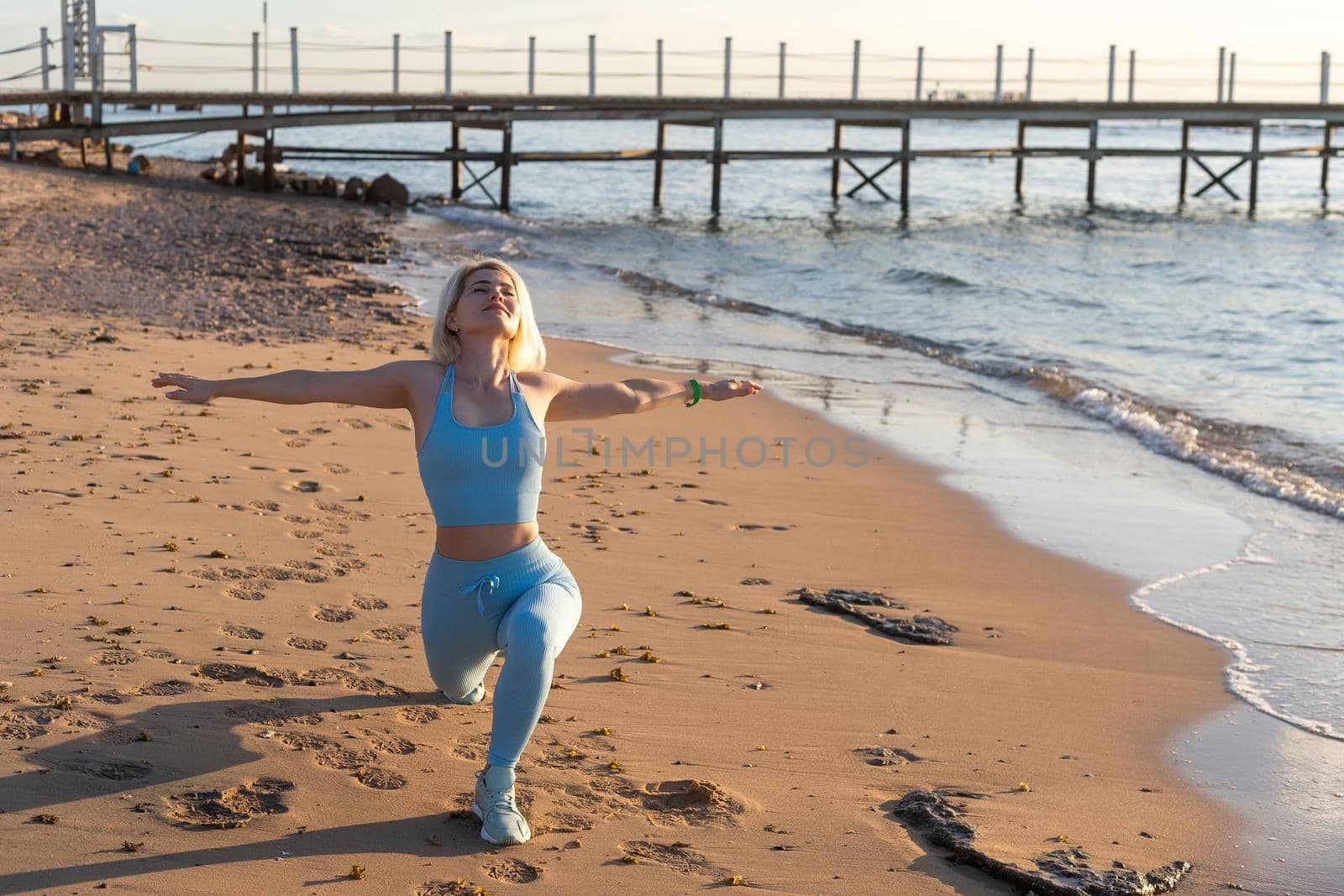 Young beautiful sportive girl training at sunrise over seaside. by Andelov13