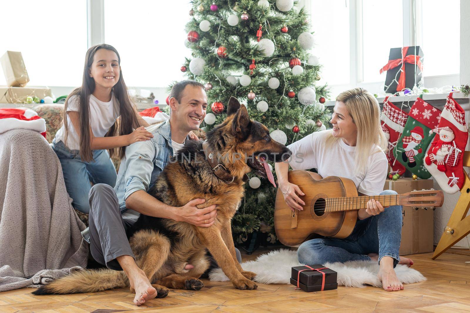 Merry Christmas and Happy New Year. Happy family with dog are waiting for the New Yearwhile sitting near beautiful Christmas tree at home