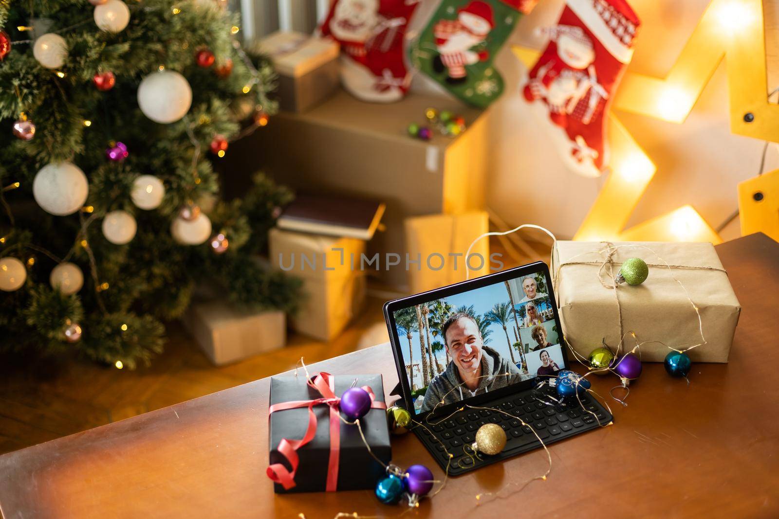 Family video call with kid presenting gift by remote chat digital tablet screen on Merry Christmas table holiday background. Xmas online virtual family party celebration, Happy New Year videocall by Andelov13