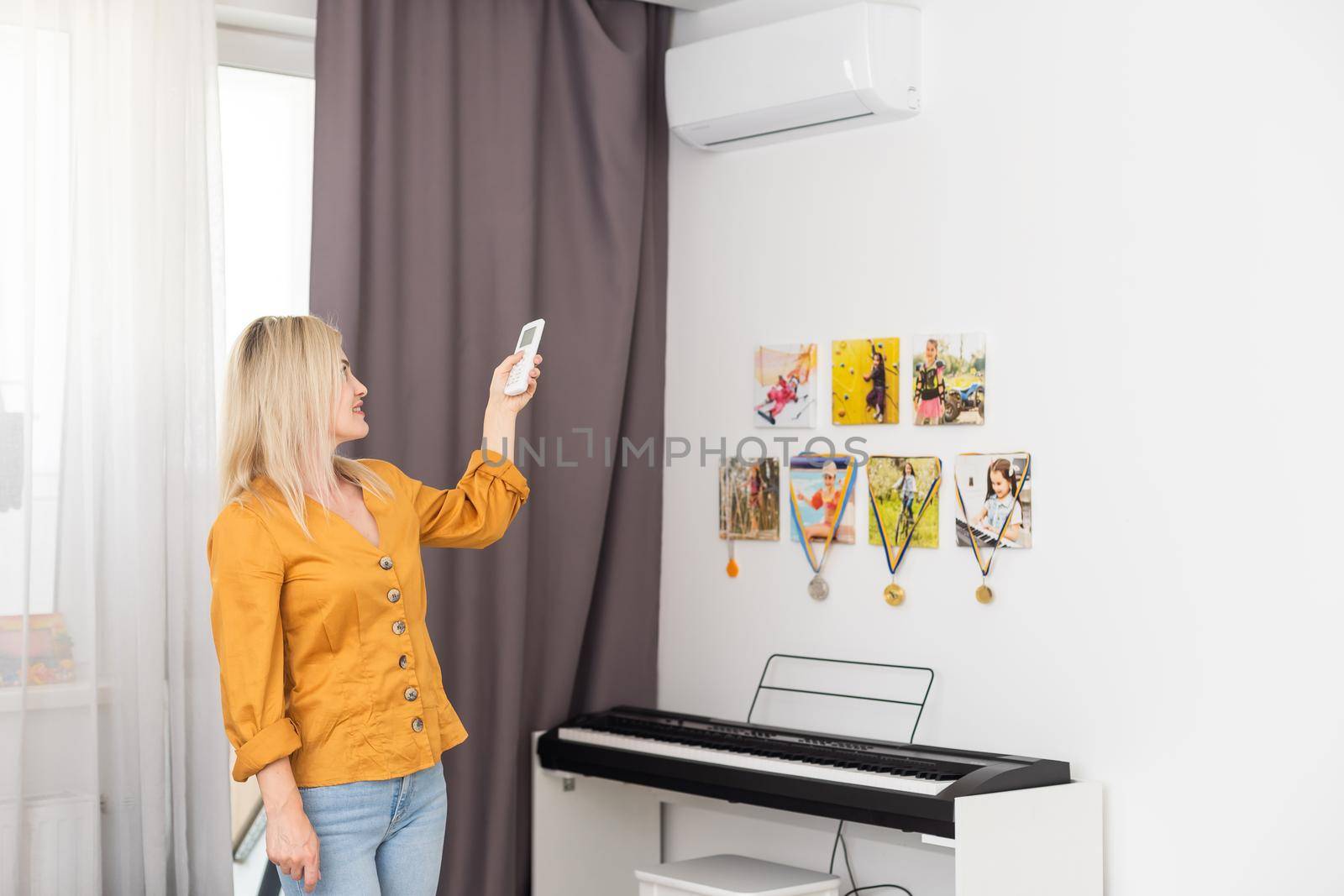 Portrait Of Smiling Young Woman Holding Remote Controller Of Air Conditioner At Home