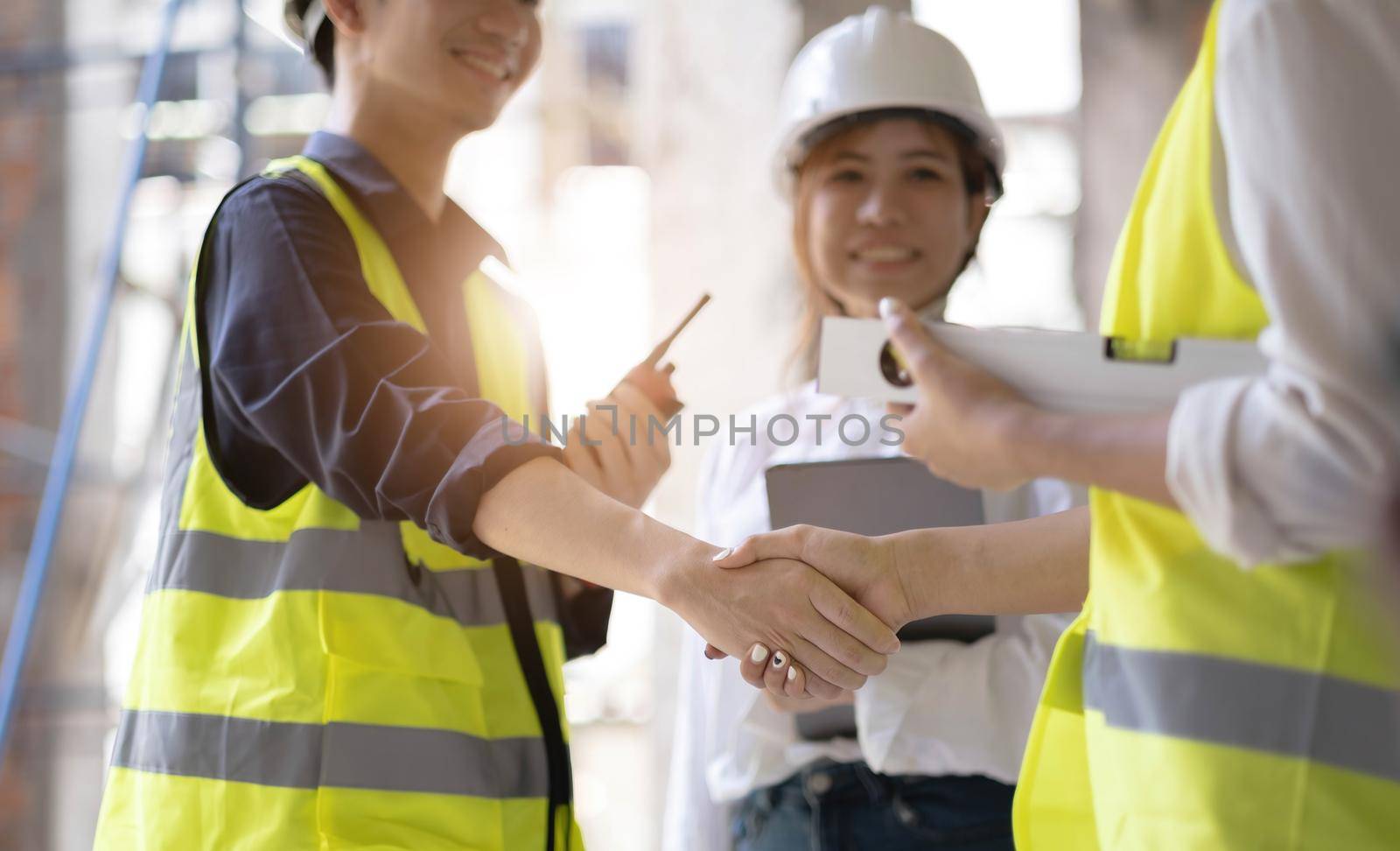 Smiling civil engineer shaking hands at construction site with businesswoman. Construction manager and supervisor shaking hand on building site. Team of workers conclude an agreement with an handshake by wichayada