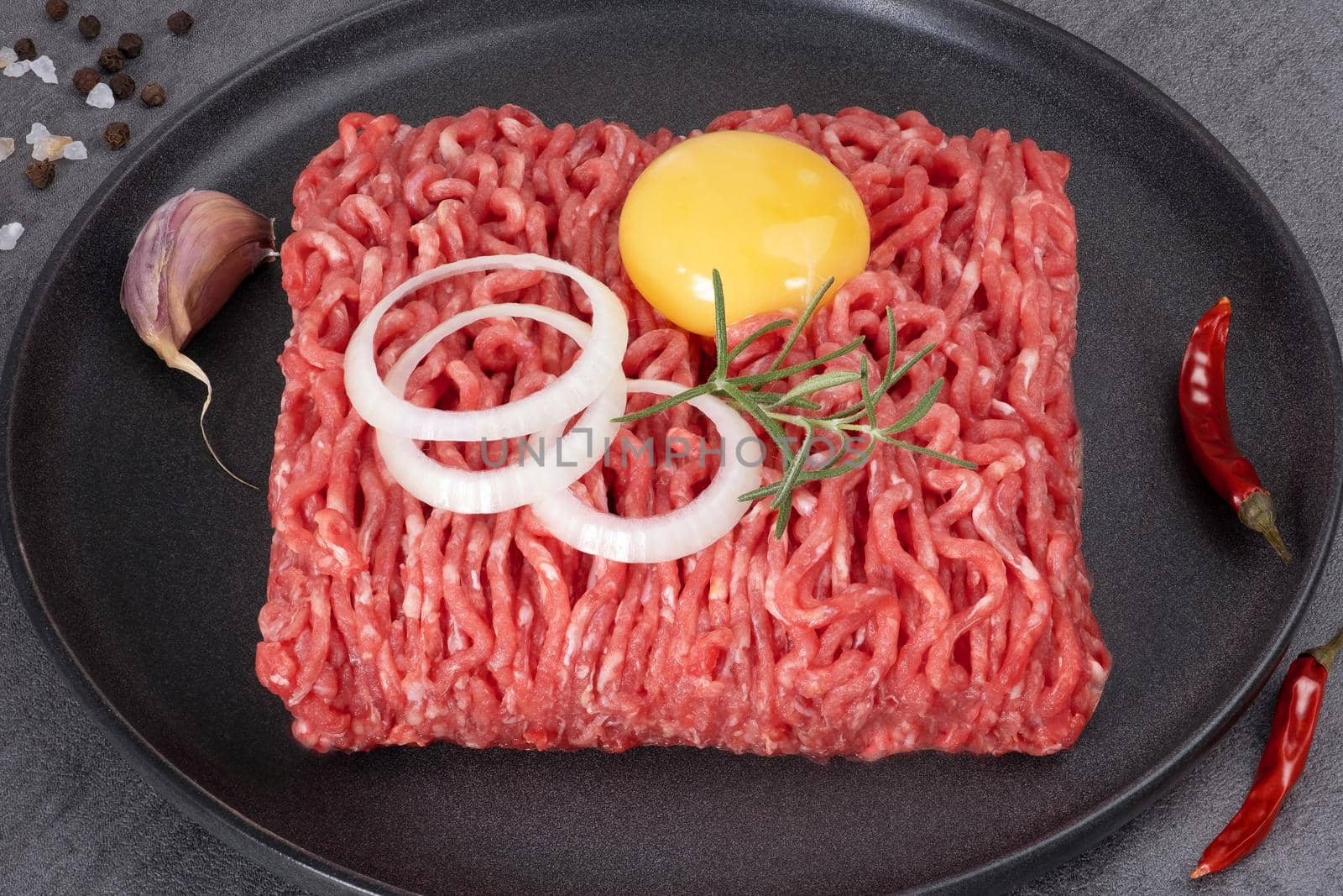 Minced meat lies on a black ceramic plate. Selective focus.