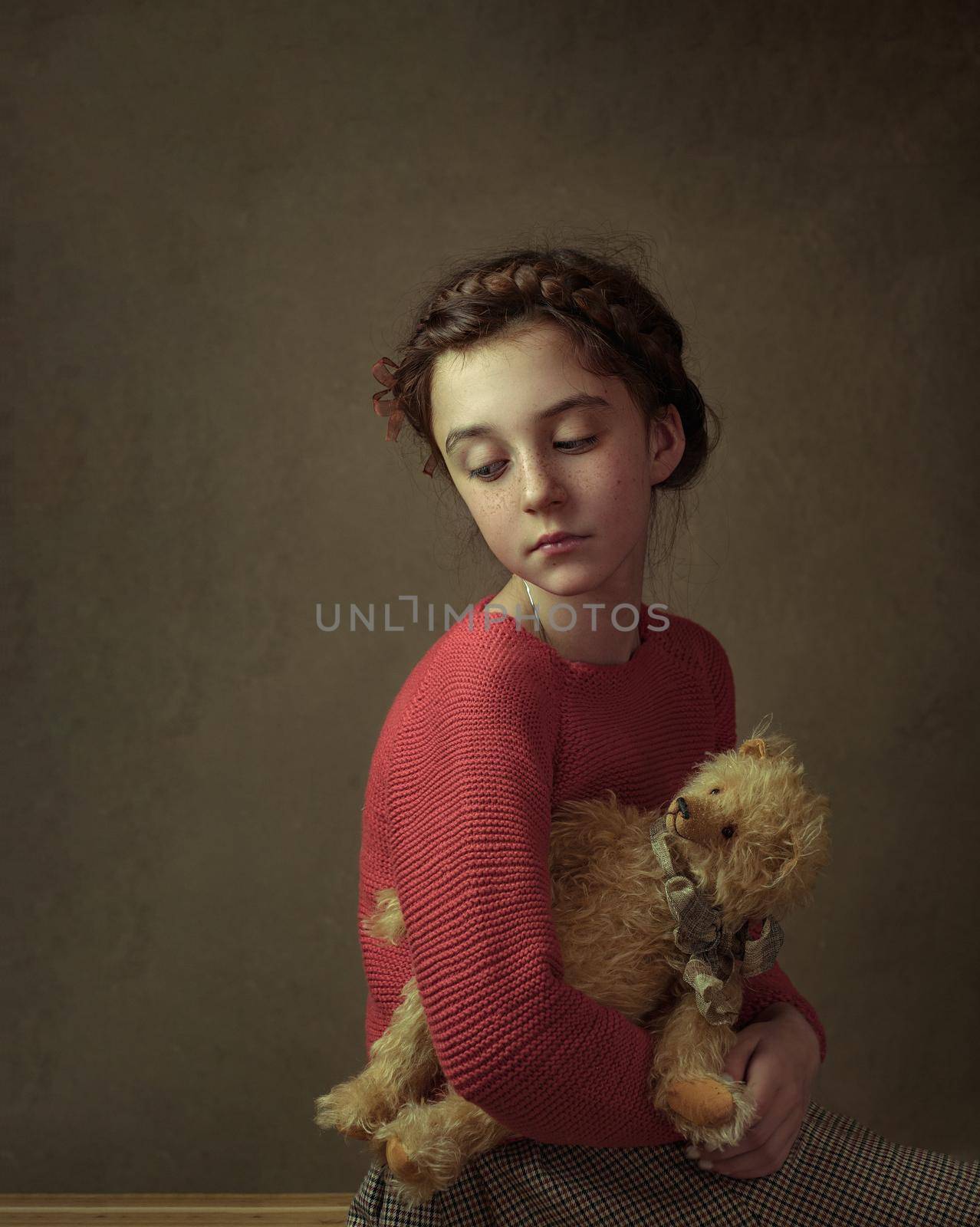 a girl with dark hair and a pigtail around her head in a red sweater is standing and holding her teddy bear toy in her hands by Costin