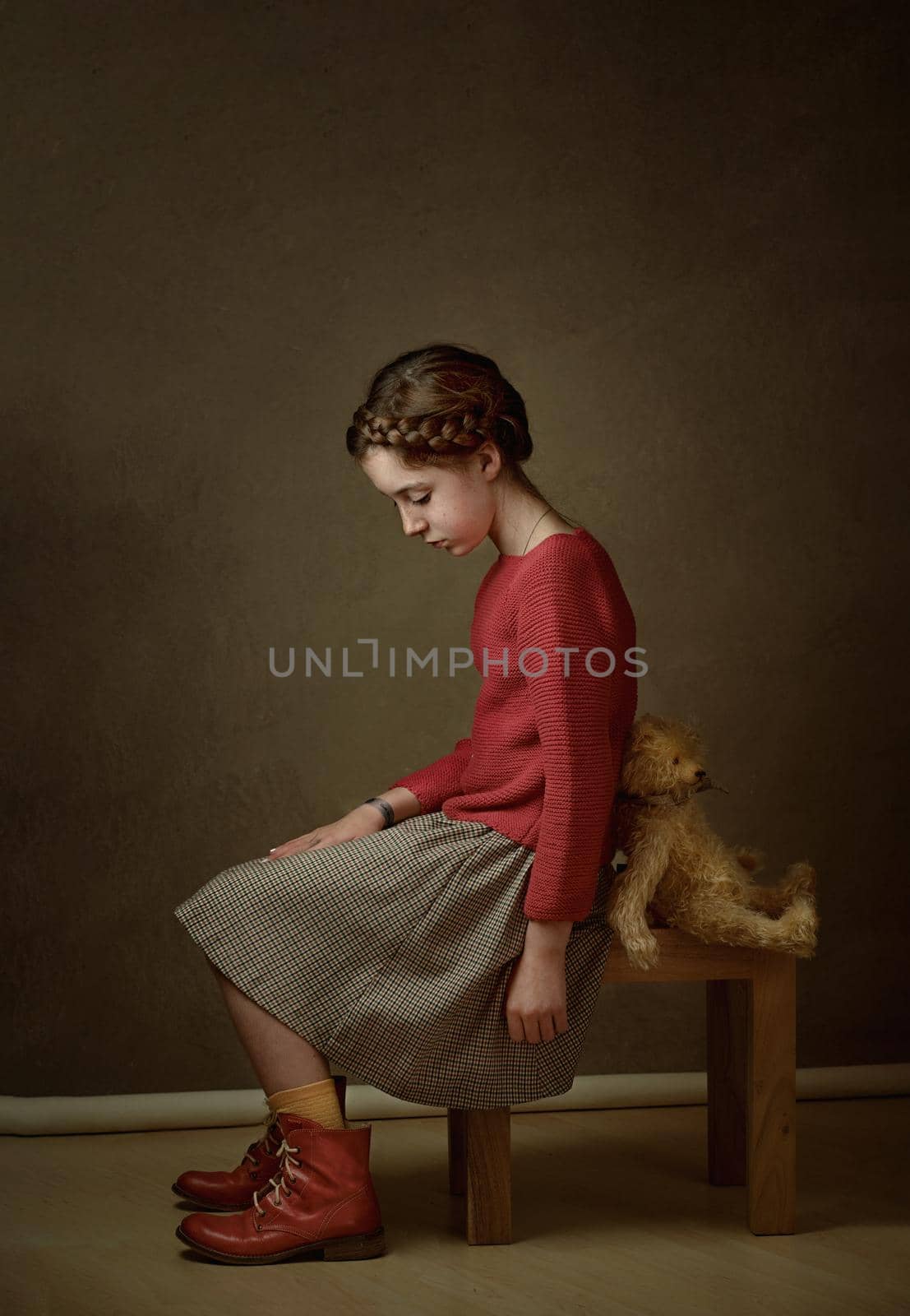 a girl with dark hair and a pigtail around her head in a red sweater is sitting with her teddy bear toy back to back offended at each other by Costin