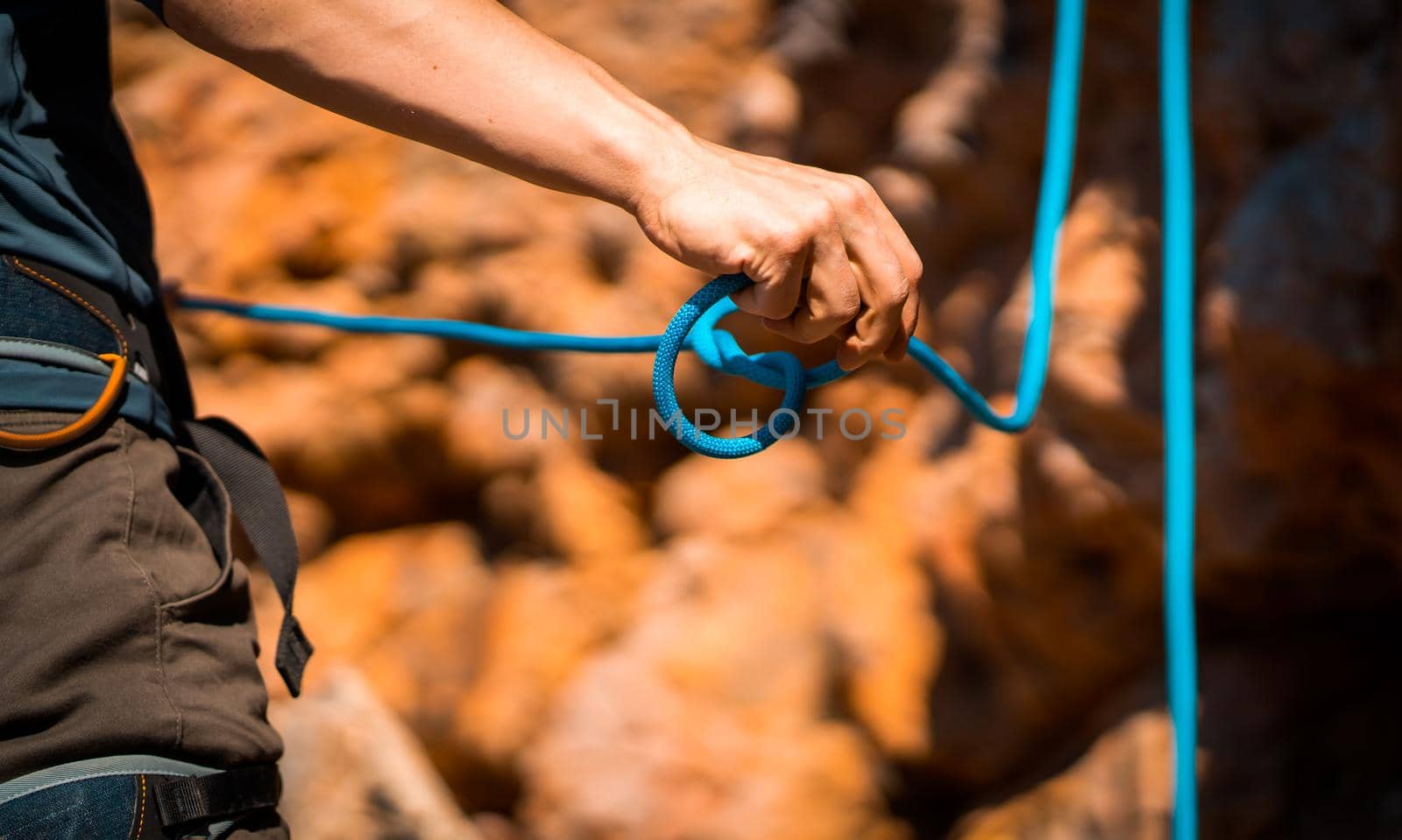 A young man prepares for rock climbing in the mountains outdoor, an athlete ties a figure eight loop on a rope during training, mountaineering on a sunny day, close-up view.