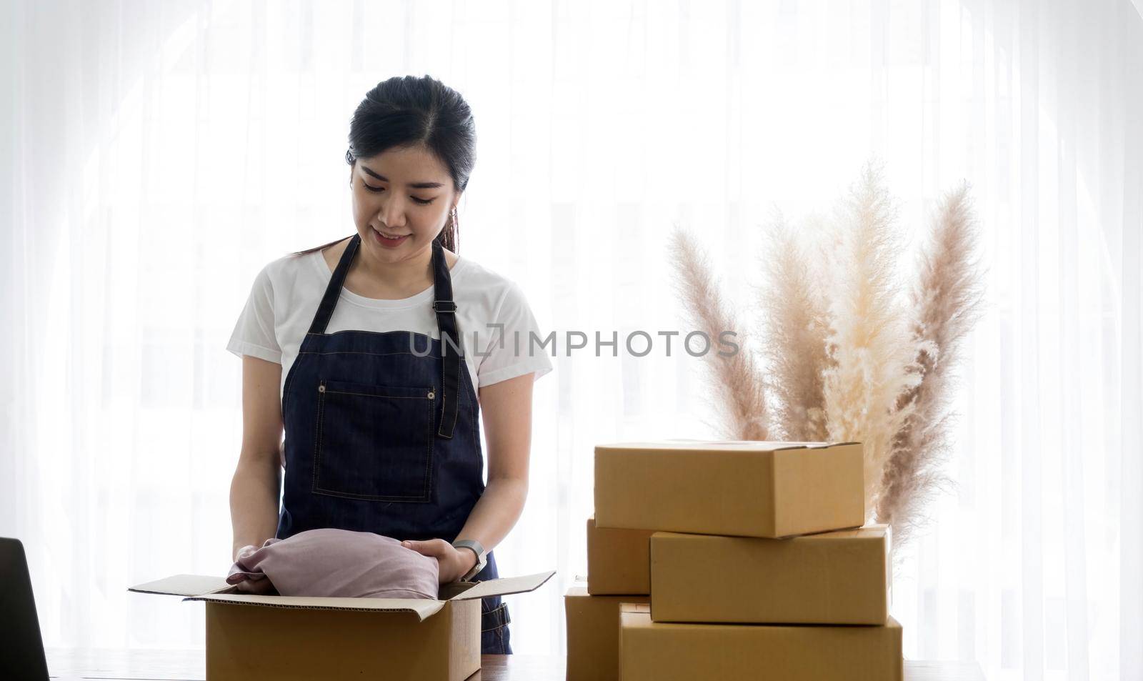 Startup small business entrepreneur SME, asian woman packing shirt in box. Portrait young Asian small business owner home office, online sell marketing delivery, SME e-commerce telemarket job concept.