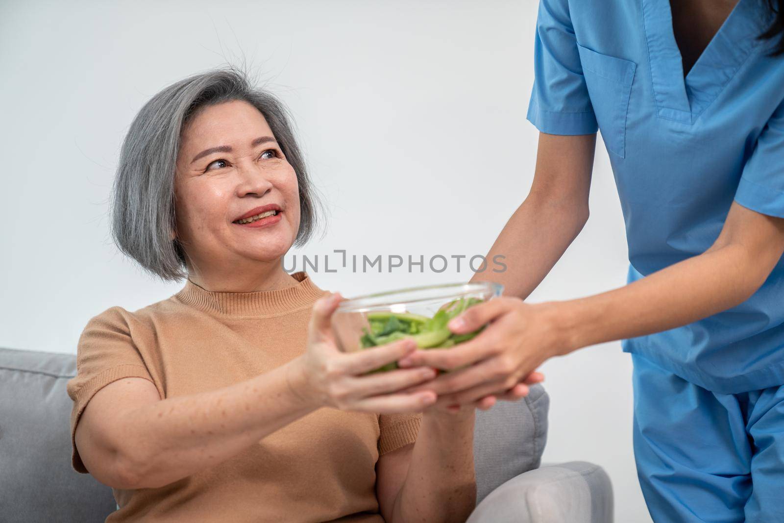 A female nurse serves a bowl of salad to a contented senior couple. by biancoblue