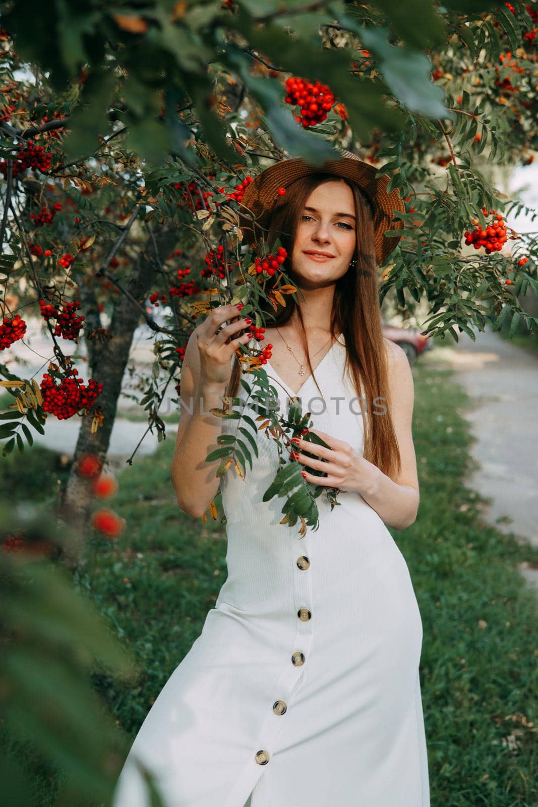 A beautiful blonde girl in a hat with long hair, on a walk in the autumn season. Portrait of a woman at a rowan tree.