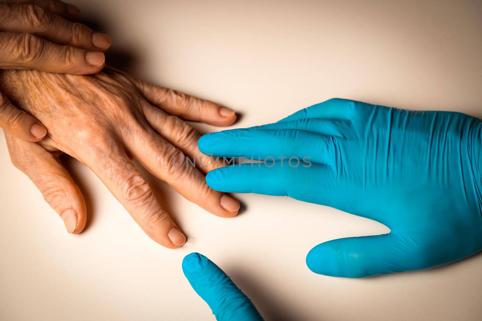 Doctor's hands in a blue gloves holds the hands of an elderly woman, a patient. Handshake, caring, trust and support. Medicine and healthcare.