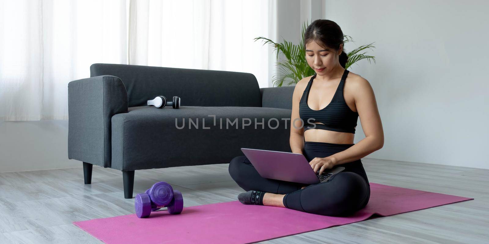 Woman using laptop while exercising at home. Female in sportswear sitting on floor and watching exercise video for her workout. by wichayada