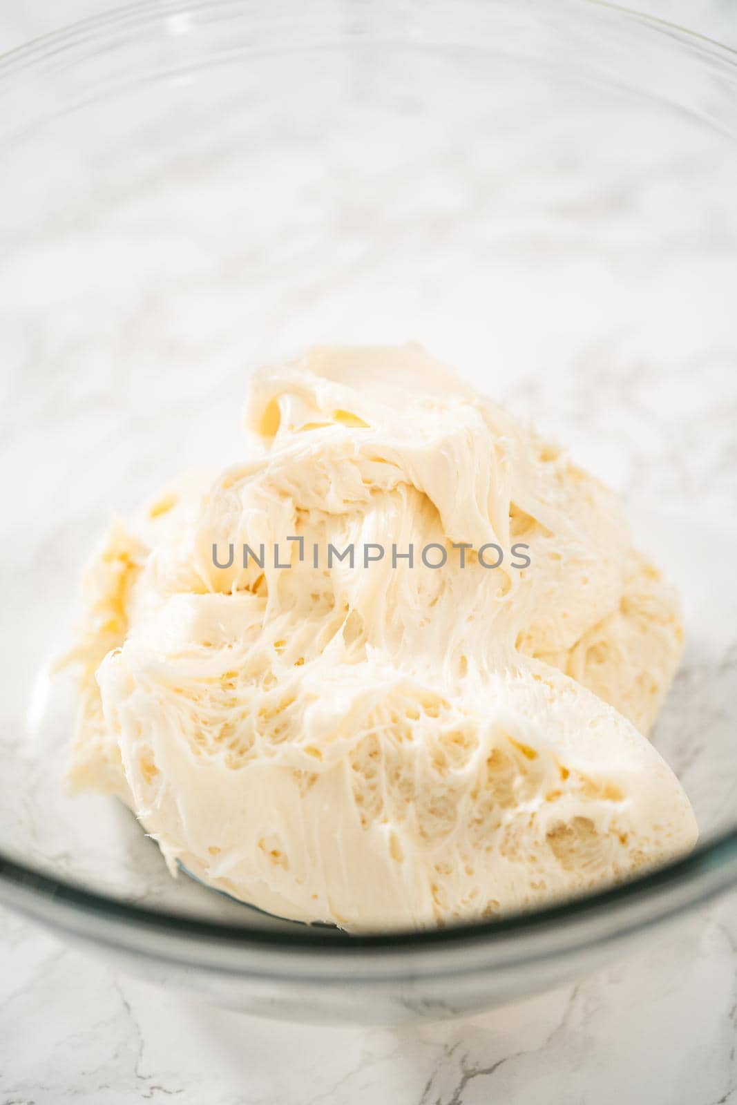 Whisking buttercream frosting in a glass mixing bowl with an electric hand mixer to prepare the peppermint buttercream frosting.