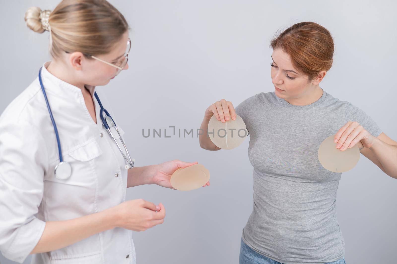 Caucasian woman trying on breast implants. A plastic surgeon helps a patient with a choice. by mrwed54