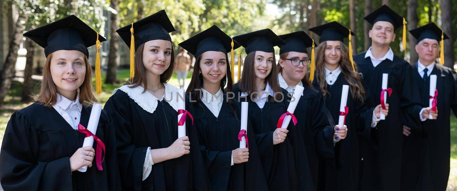 Row of young people in graduation gowns outdoors. Age student. Widescreen