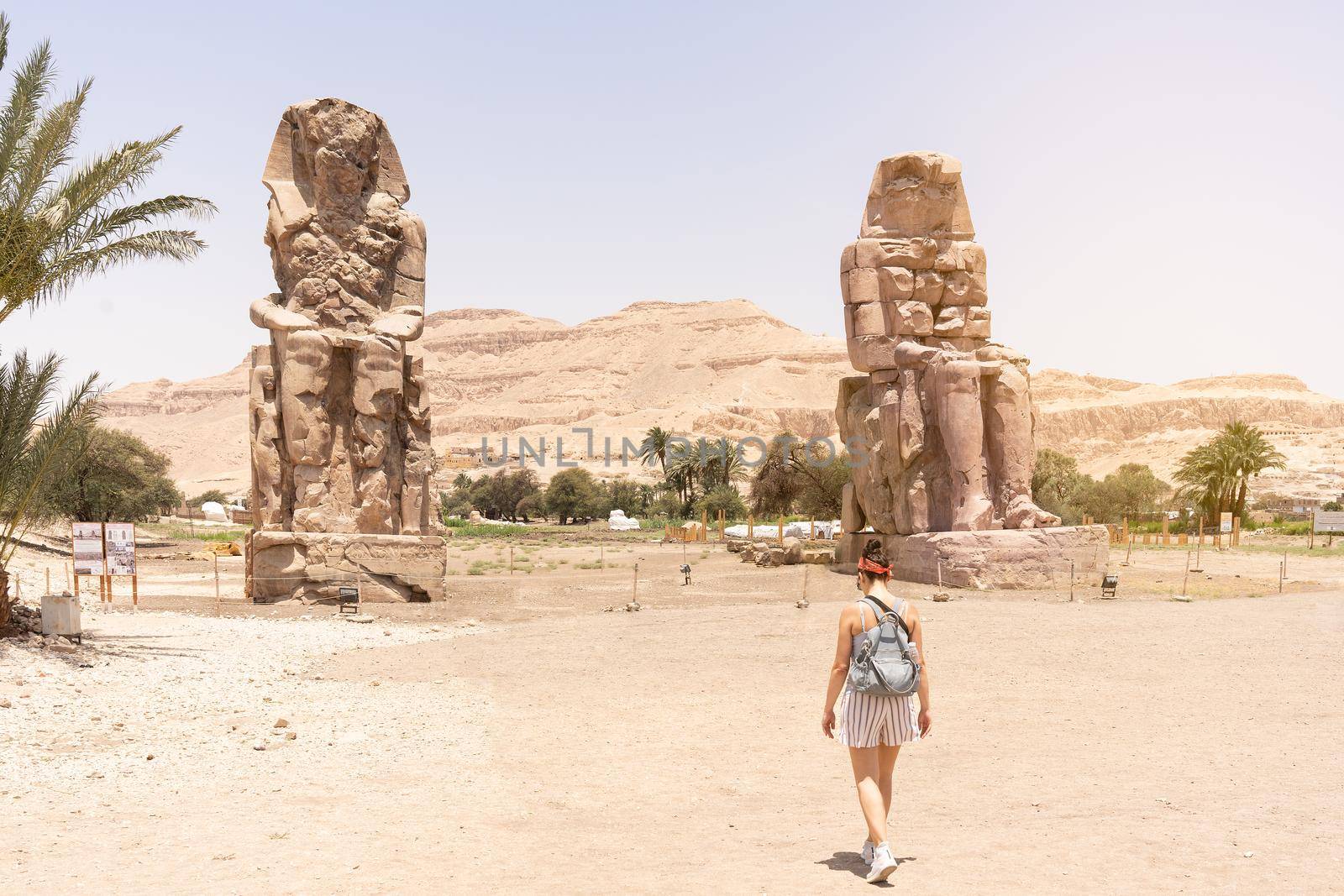 Female tourist walking towards the ancient egyptian statues of the Pharaoh Amenophis. Colossi of Memnon.