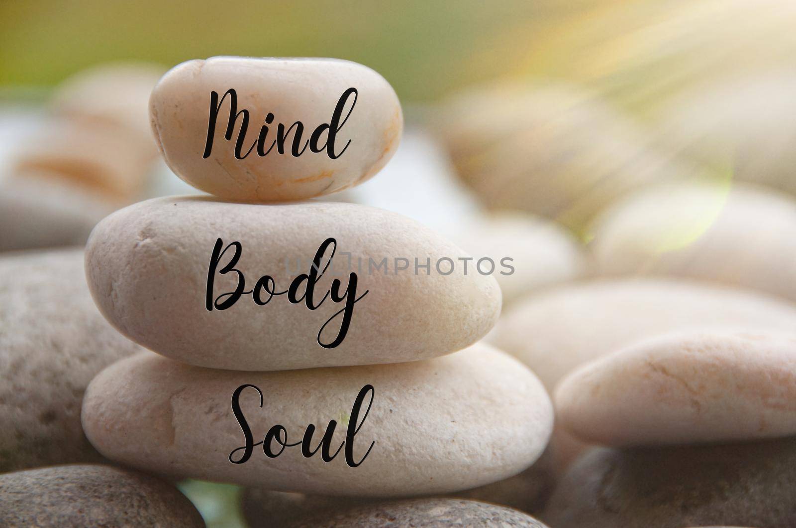 Light shining on zen stones with words Mind, Body, Soul on blurred background. Customize space for text or ideas by yom98