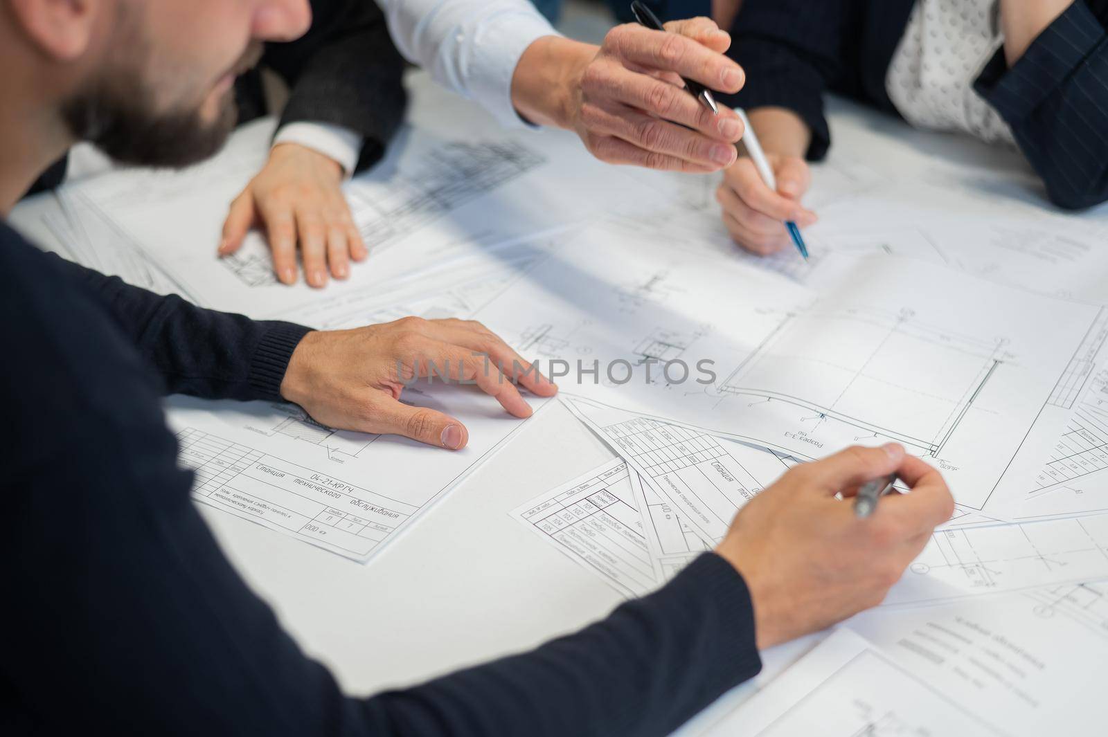 Close-up of the hands of four colleagues with blueprints on the table in the office. Brainstorming of engineers and architects