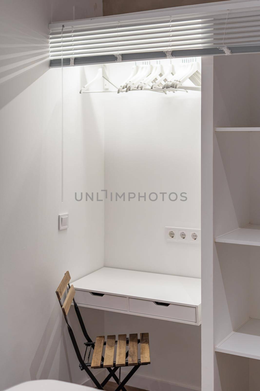 White study table combined with wardrobe with wooden shelves and a chair in a small student room for rent. by apavlin