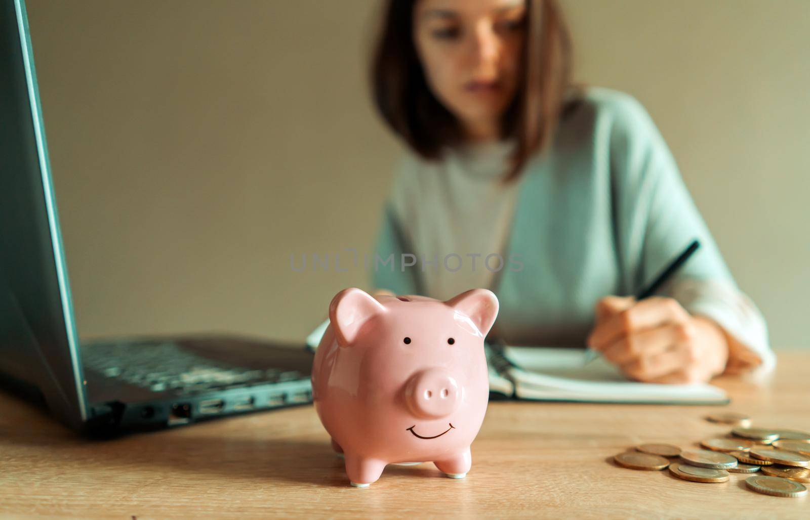 A young girl makes calculations, checks her finances, makes notes in a notebook and sets aside some of the funds, savings in a piggy bank for personal expenses and future development.