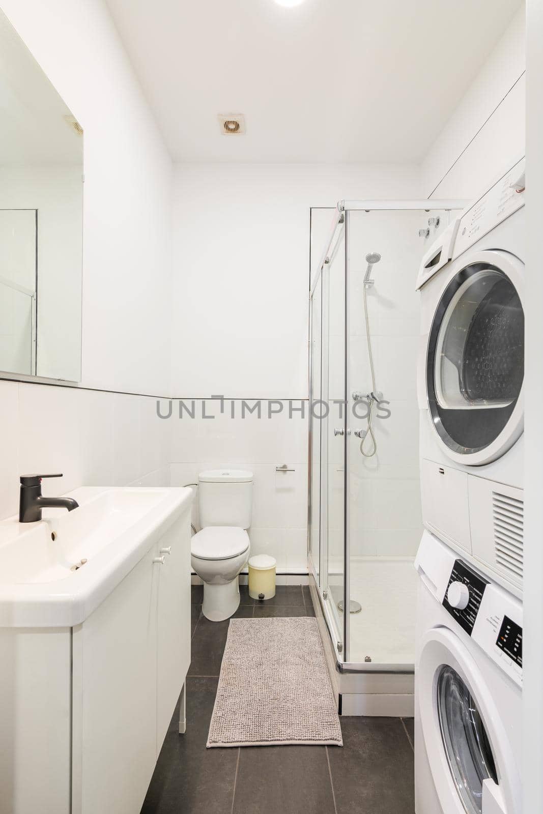 Small and narrow white bathroom with shower cabin, washing machine and dryer by apavlin
